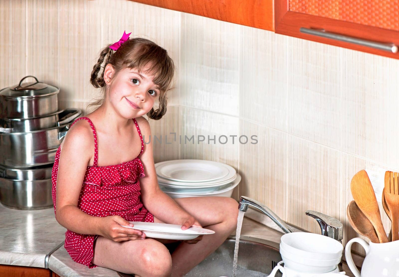 The concept of mother's helper, child development, family. Little girl washes white dishes at home in the kitchen by aprilphoto