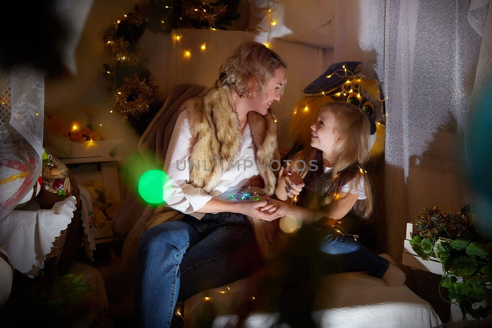 Cute mother and daughter in a room with Christmas garlands. The tradition of decorating the house and dressing up for the holidays. Gifts for family. Happy childhood and motherhood