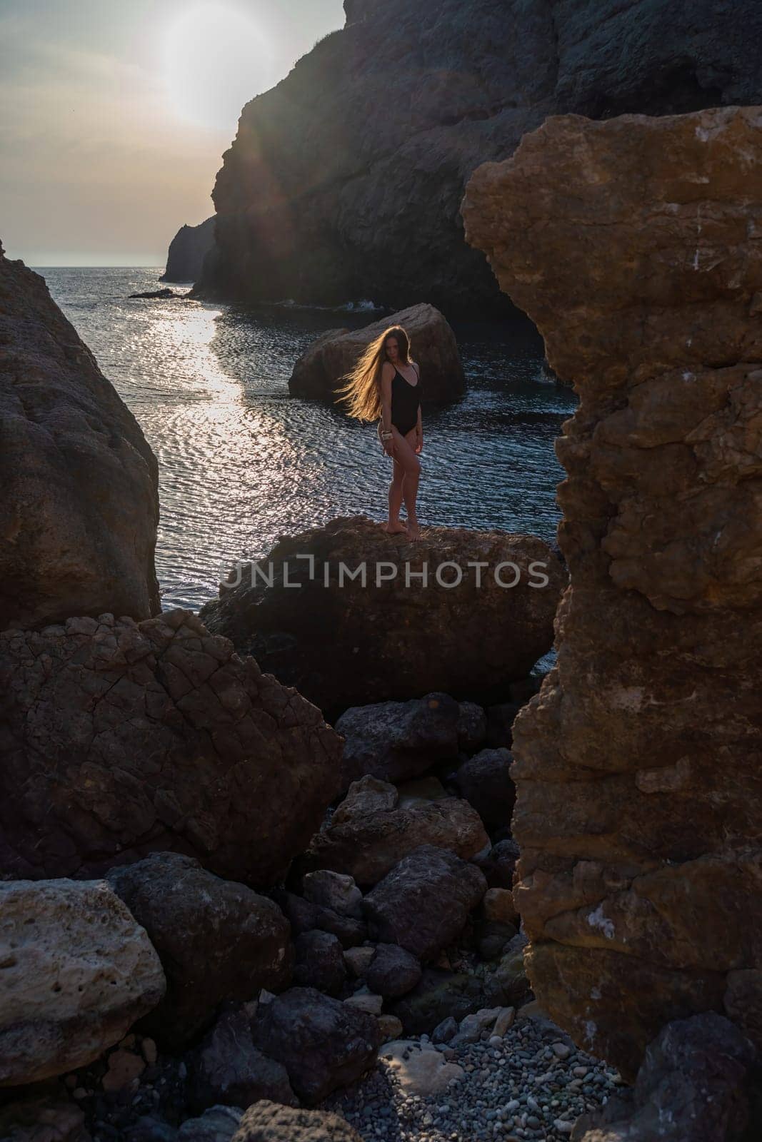 Woman tourist enjoying the sunset over the sea mountain landscape. Sits outdoors on a rock above the sea. She is wearing jeans and a blue hoodie. Healthy lifestyle, harmony and meditation.