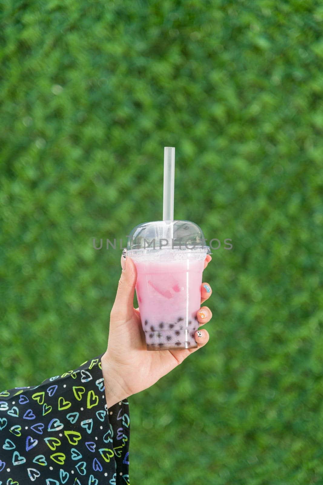 Woman holding bubble tea with lemonade in front of green grass wall by Sonat