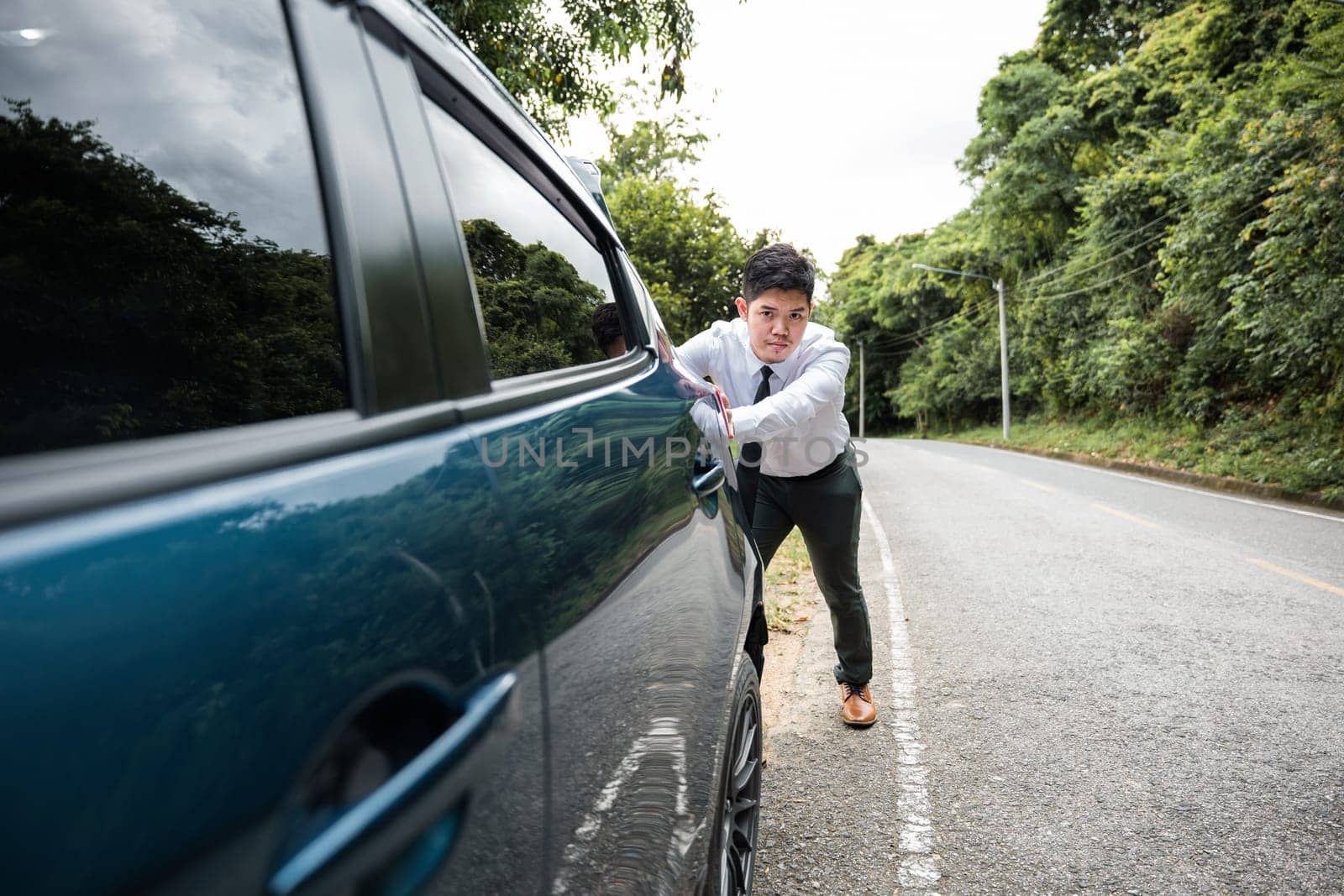 Asian businessman car broken has problems with car down during go to work in morning he pushing out of gas on road at countryside, business man have trouble roadside, problem transportation