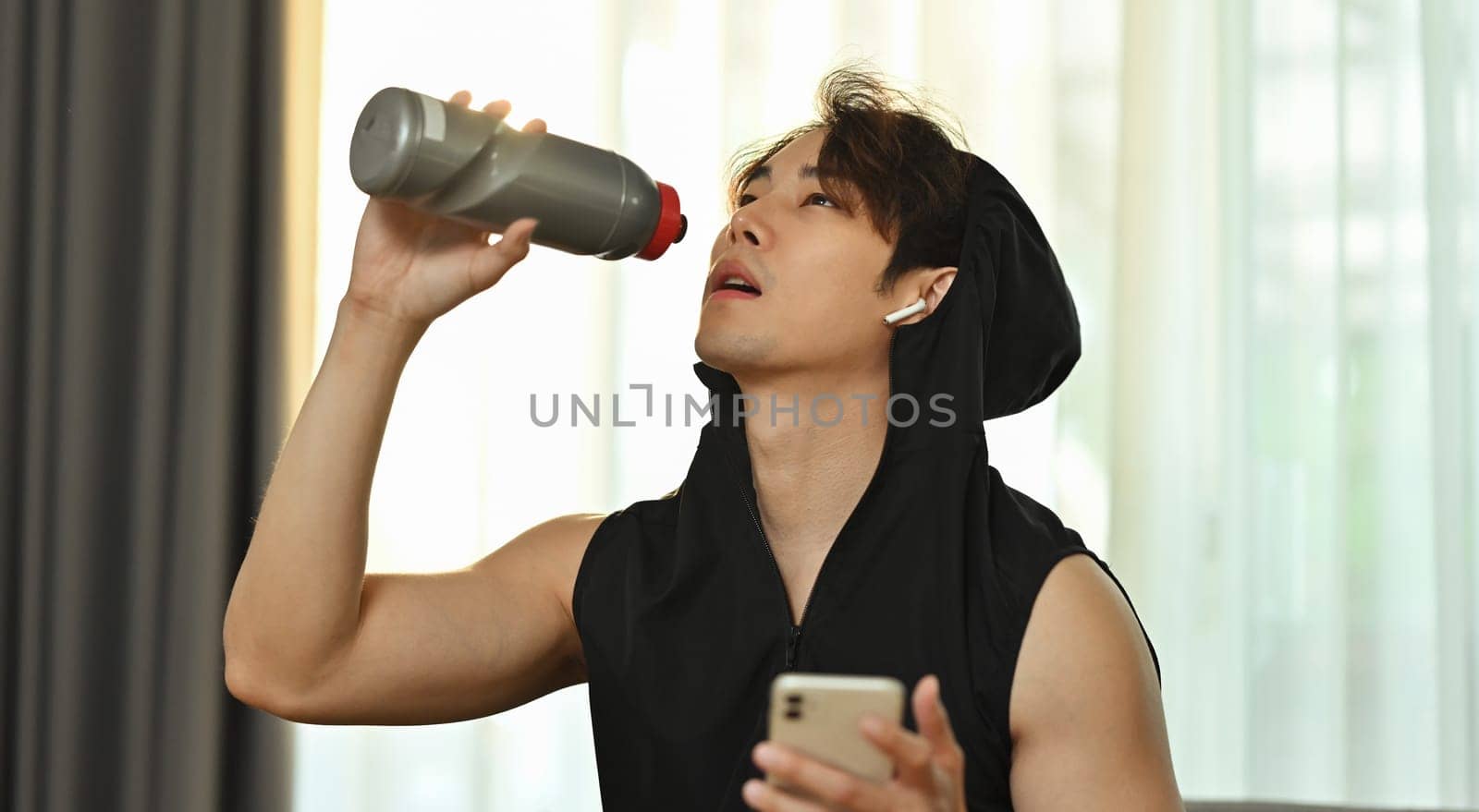 Young sportsman drinking water from bottle, resting after home workout session. Fitness, training and healthy lifestyle.