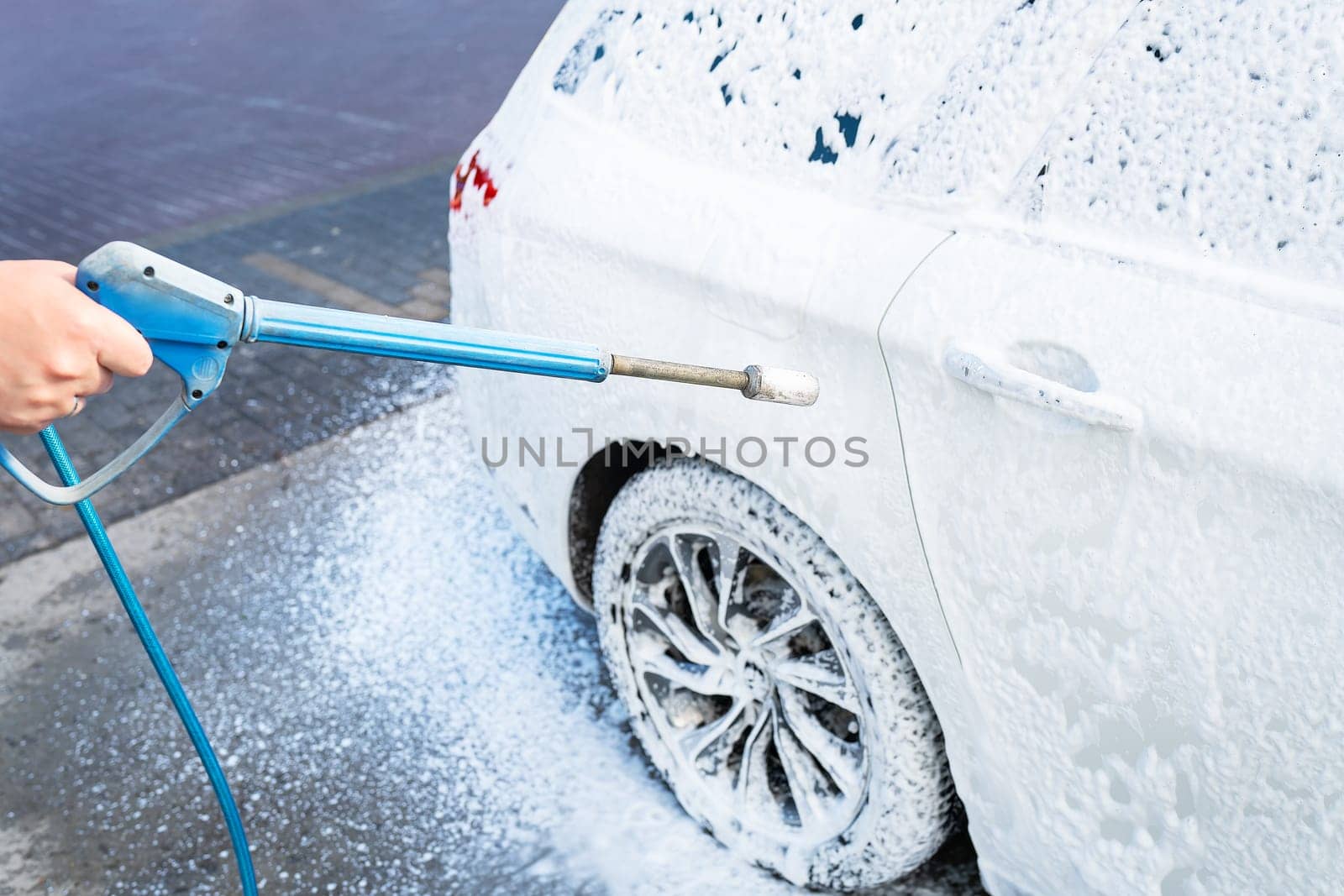 Hand washing with high pressure water in a car wash outside. A jet of foam. The concept of hand washing, self-service