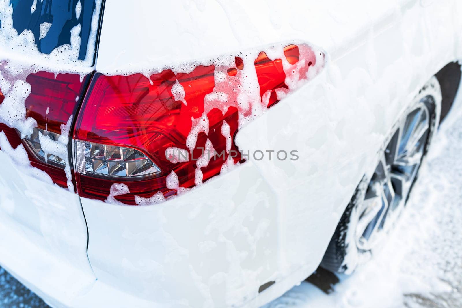 Hand washing with high pressure water in a car wash outside. The car is full of foam. The concept of hand washing, self-service