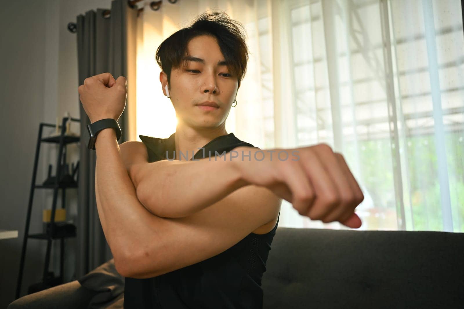 Handsome muscular man in sportswear stretching his arms, warming up exercises before working out at home by prathanchorruangsak