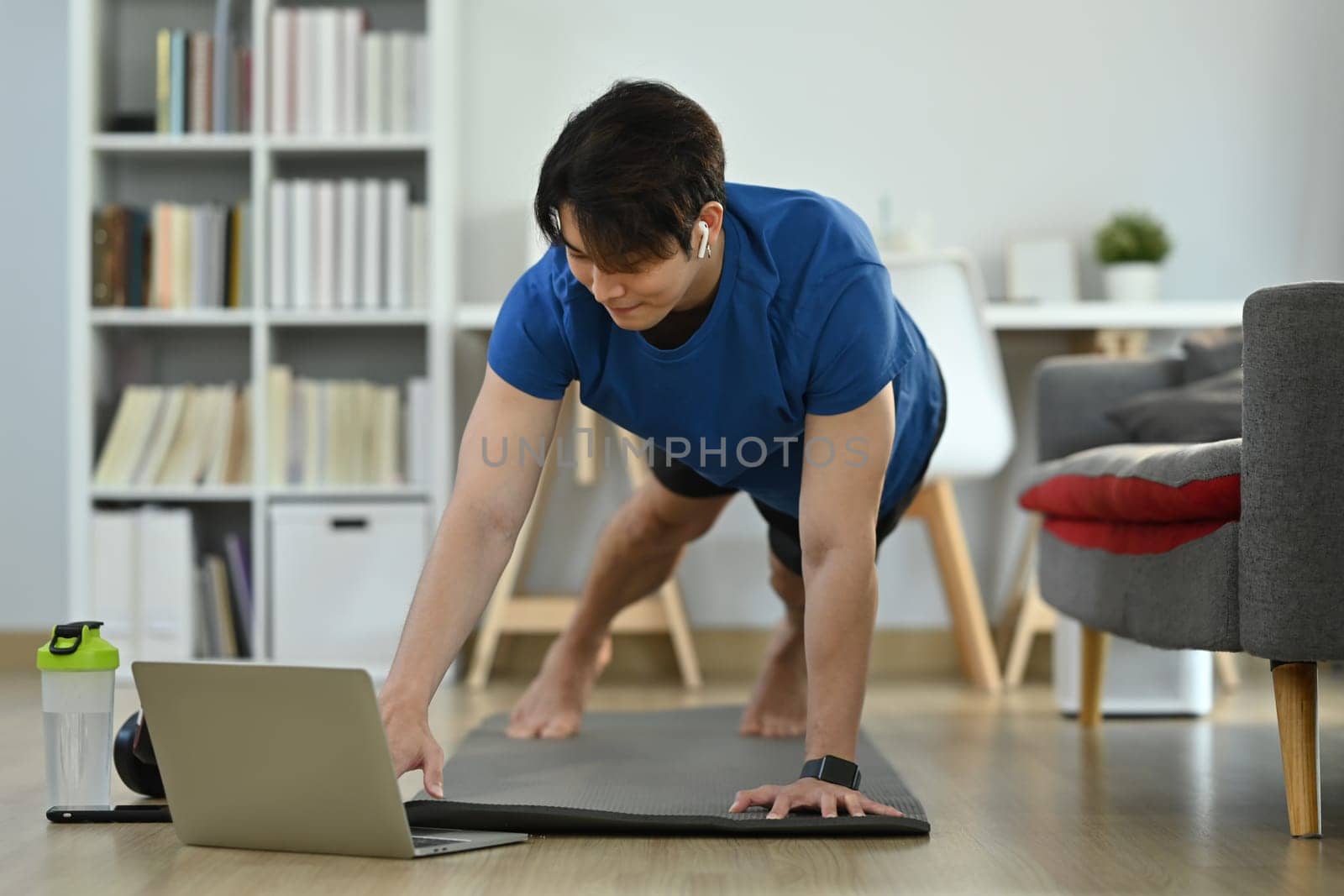 Young man in sportswear working out at home and watching fitness lessons online on laptop. Fitness, training and healthy lifestyle by prathanchorruangsak