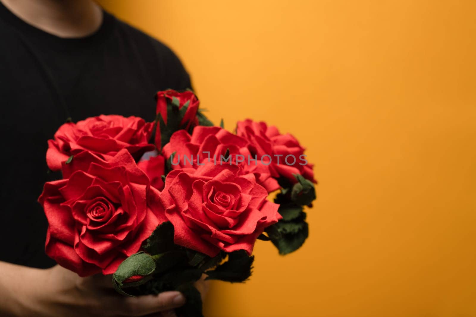 Man hands holding bouquet of red roses over yellow background with space for text by prathanchorruangsak