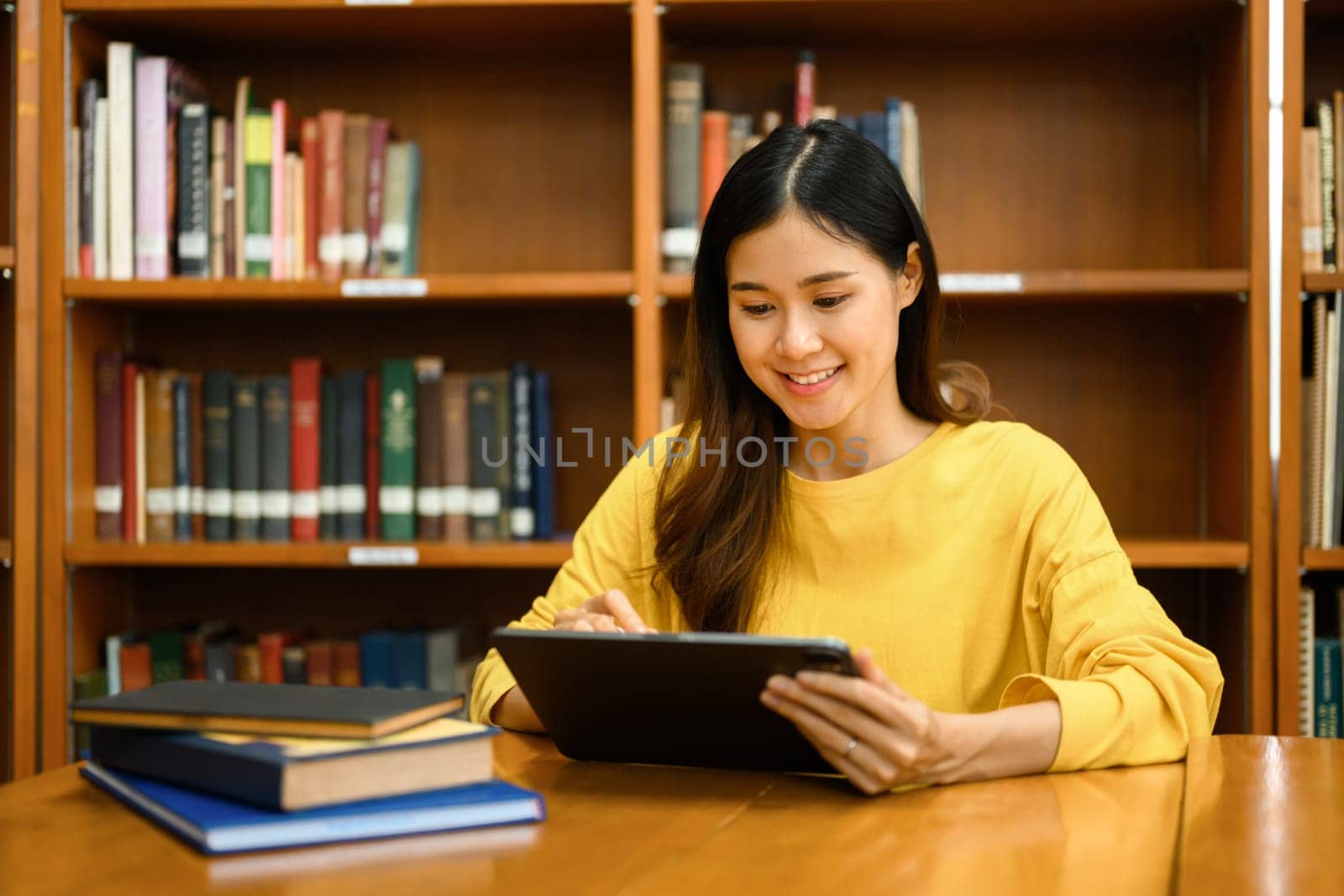 Interested asian female student using digital tablet, doing class assignment in library. Education, learning and people concept.