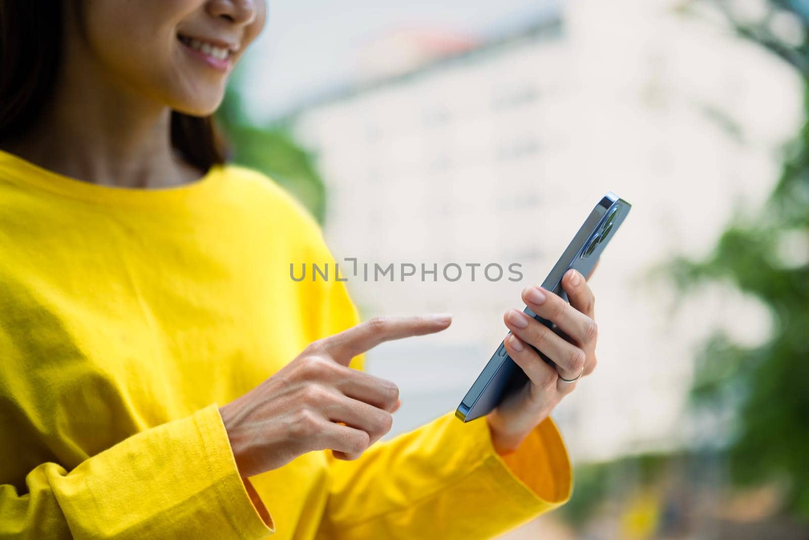 Pleasant young woman texting messages, chatting in social on smartphone while standing outdoor by prathanchorruangsak