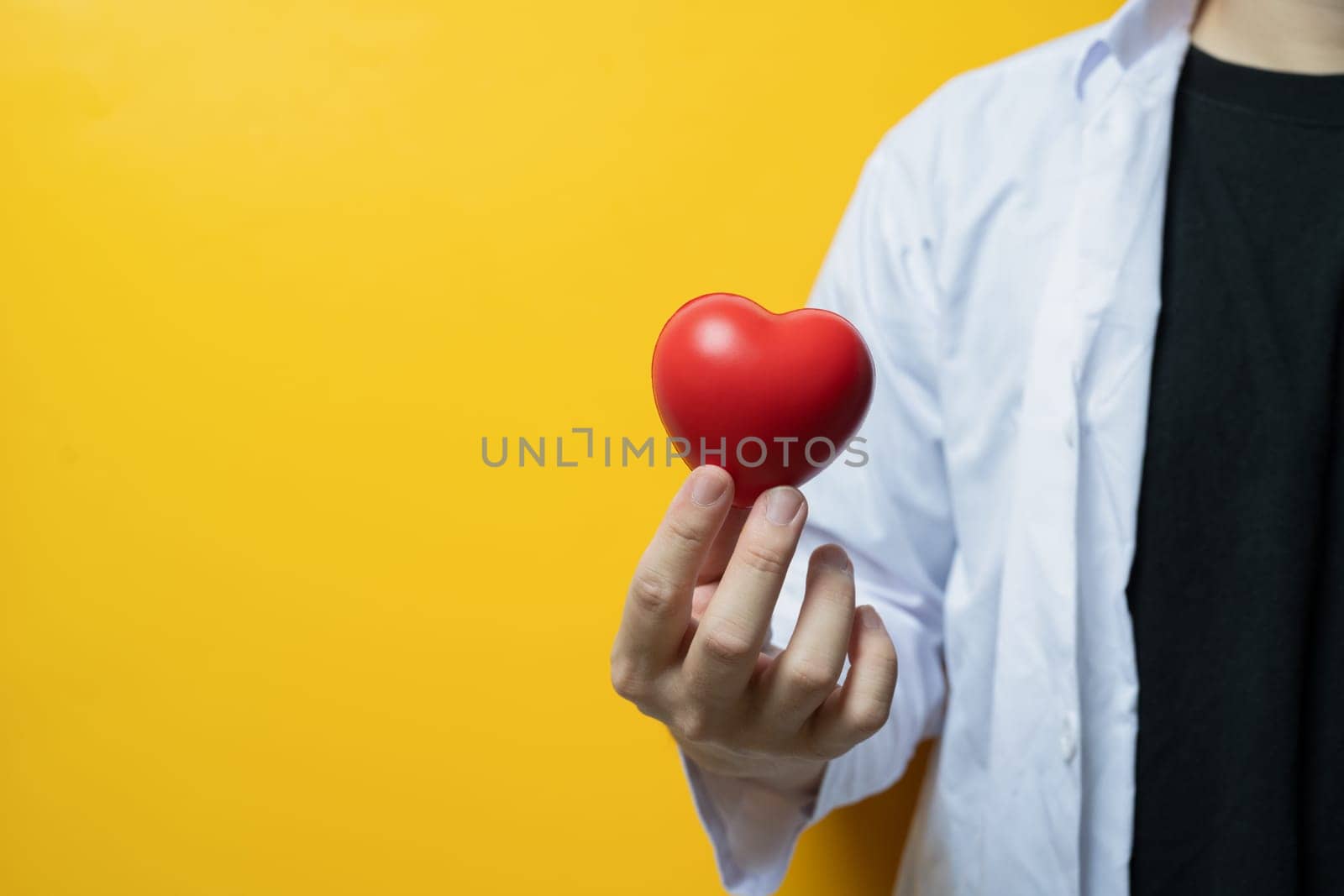 Doctor hand holding red heart on yellow background Cardiology, medicine, donation and healthcare concept.