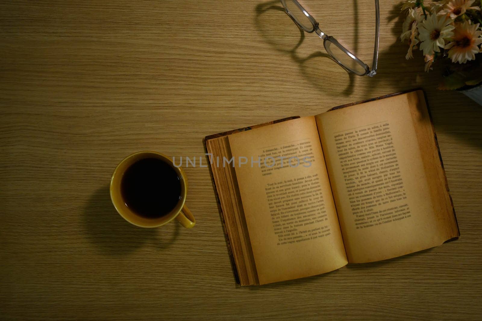 A cup of coffee, eyeglasses and open book on rustic wooden table. Top view with space for text by prathanchorruangsak