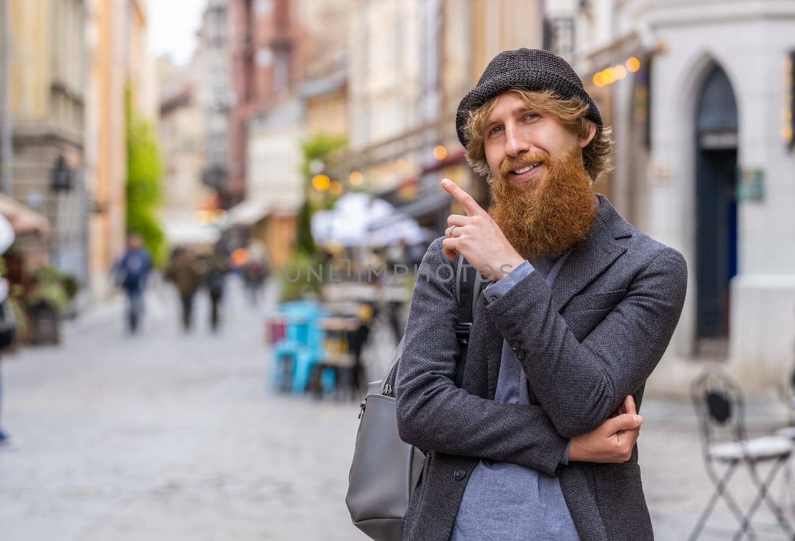 Thoughtful pensive puzzled man with pensive expression, pondering a solution, doubting question, thinking inspiration dreaming outdoors. Bearded guy in city street pointing empty place. Copy-space