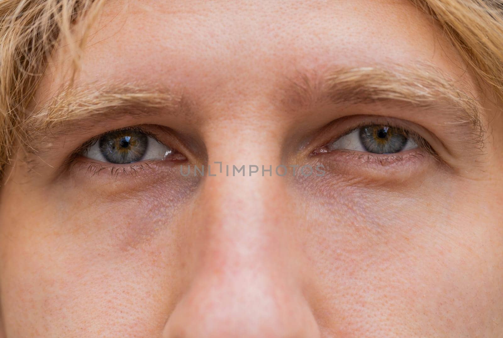 Extreme close-up macro portrait of face. Young adult beautiful redhead man's eyes looking at camera. Gray eyes of guy, red hair boy male. Caucasian man opening blinking eyes, smiling. Laser correction
