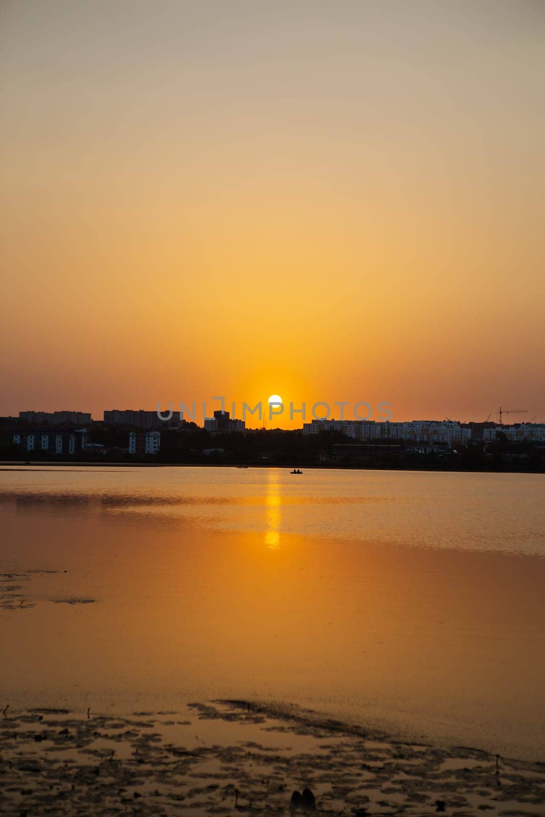 Far away, against the backdrop of a shui town, a fisherman is fishing on the lake from an inflatable small boat, against the backdrop of a beautiful orange sunset. by sfinks