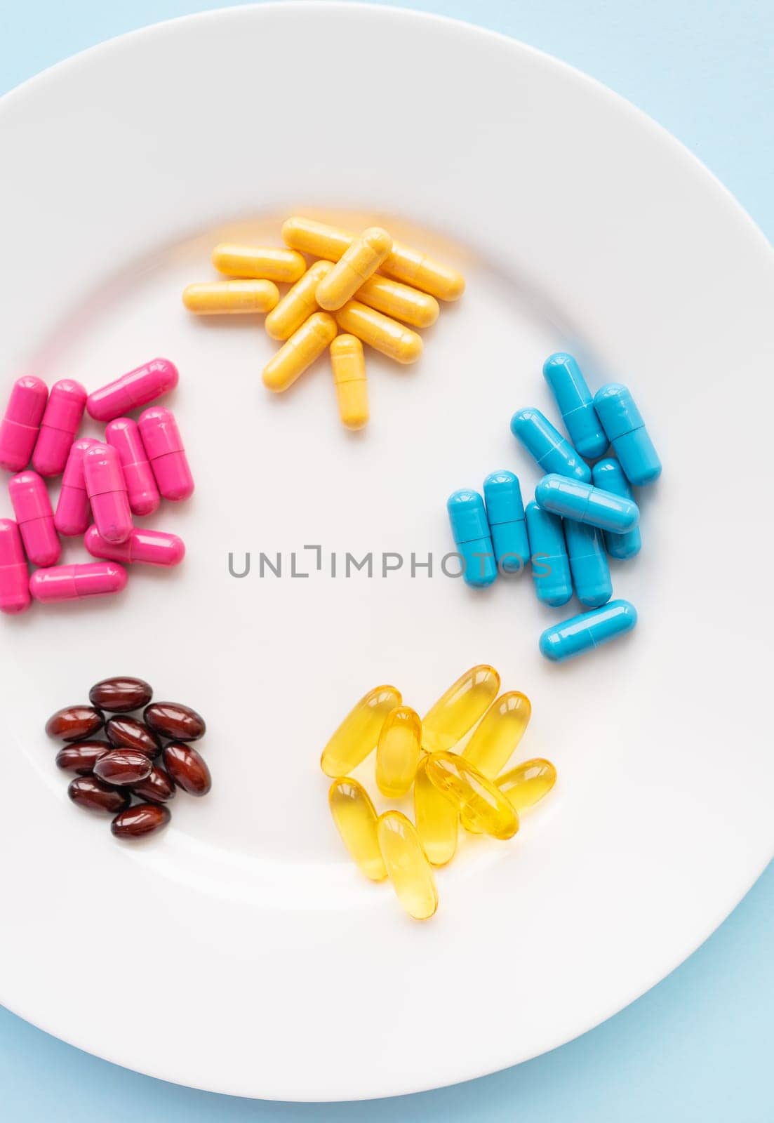 Food supplements of bright color lie on a white plate on a blue background. Concept of health support and lack of vitamins. Vertical photo. by sfinks