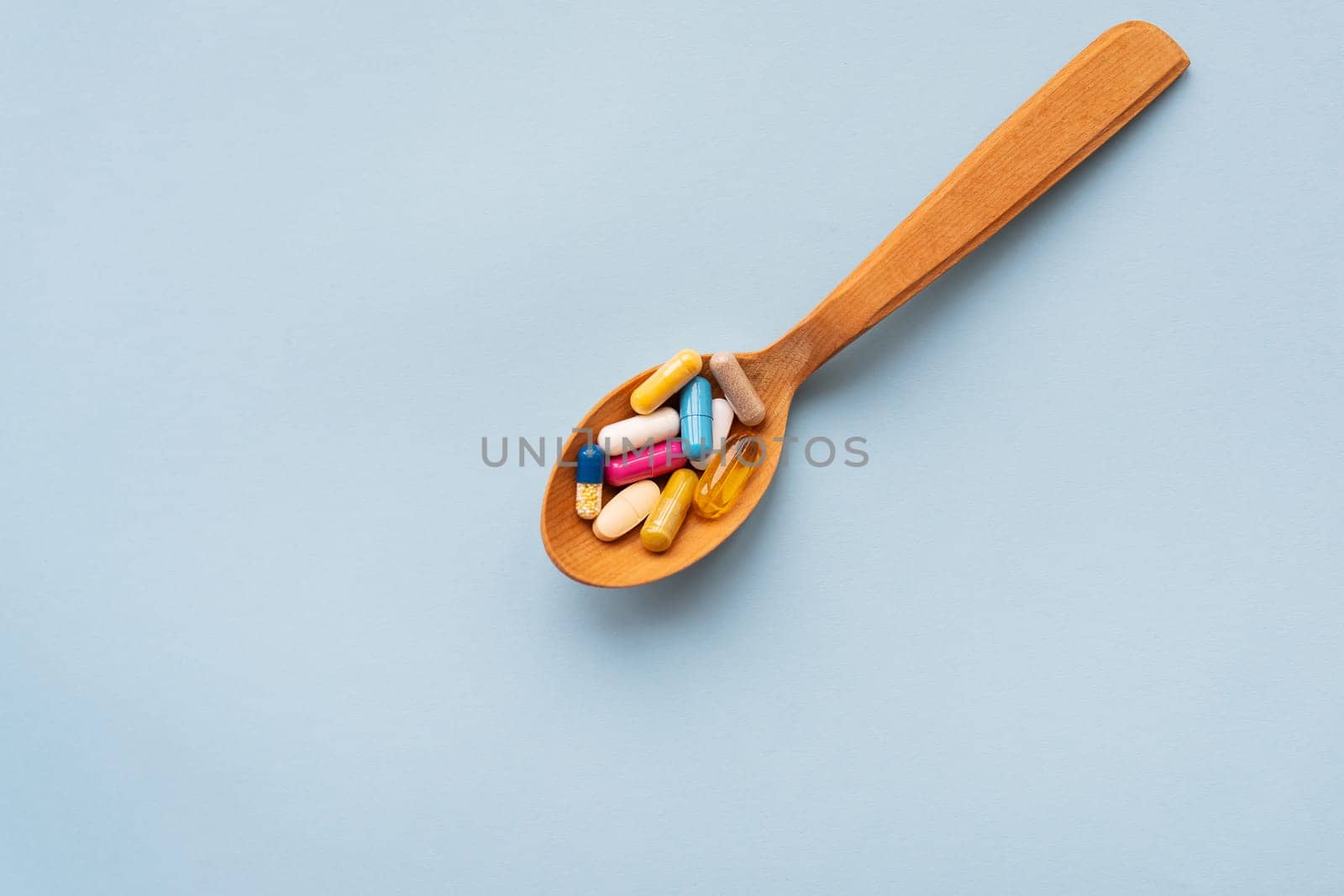 Various bright pills on a blue background lie in a wooden spoon. The concept of healthcare and evidence-based medicine, close-up