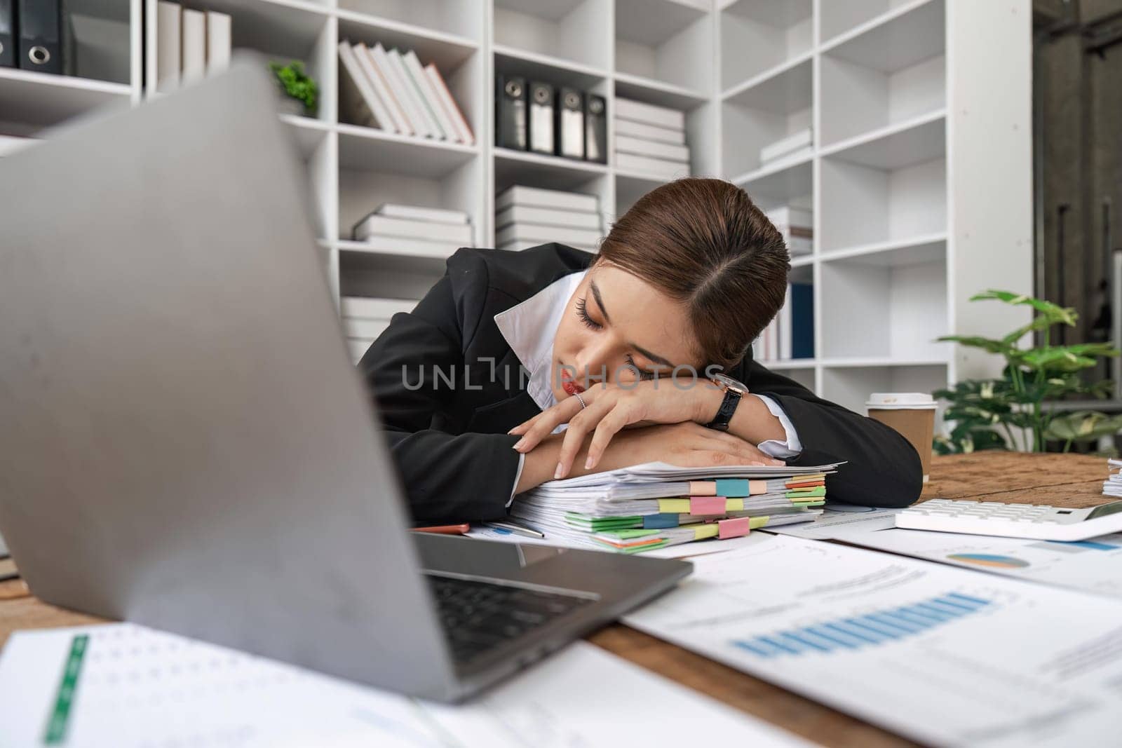 Tired or exhausted young business woman napping on working desk in front of her laptop in office.