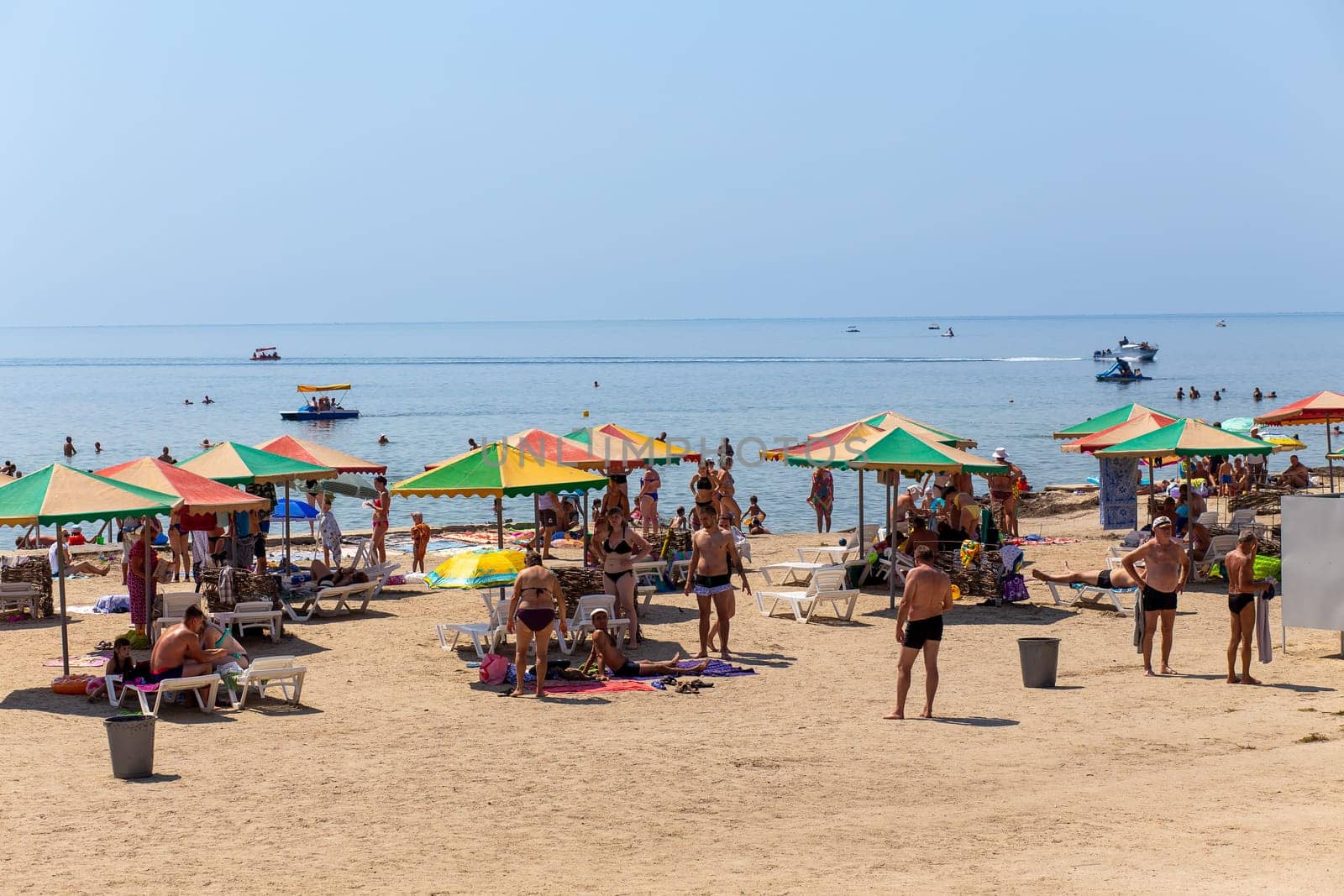 Skadovsk, Ukraine - August 15, 2018: People on beach in the Black Sea before the War. Rest on the city beaches of Skadovsk. Rows of canopies with sun beds for relaxing and sunbathing.