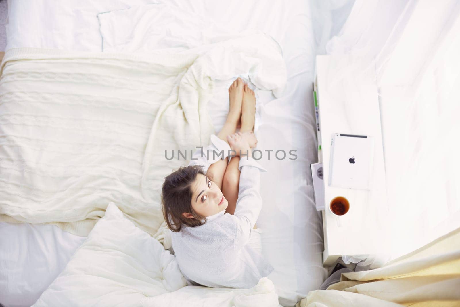 Portrait of woman using tablet and drinking coffee while sitting on the bed in the morning.