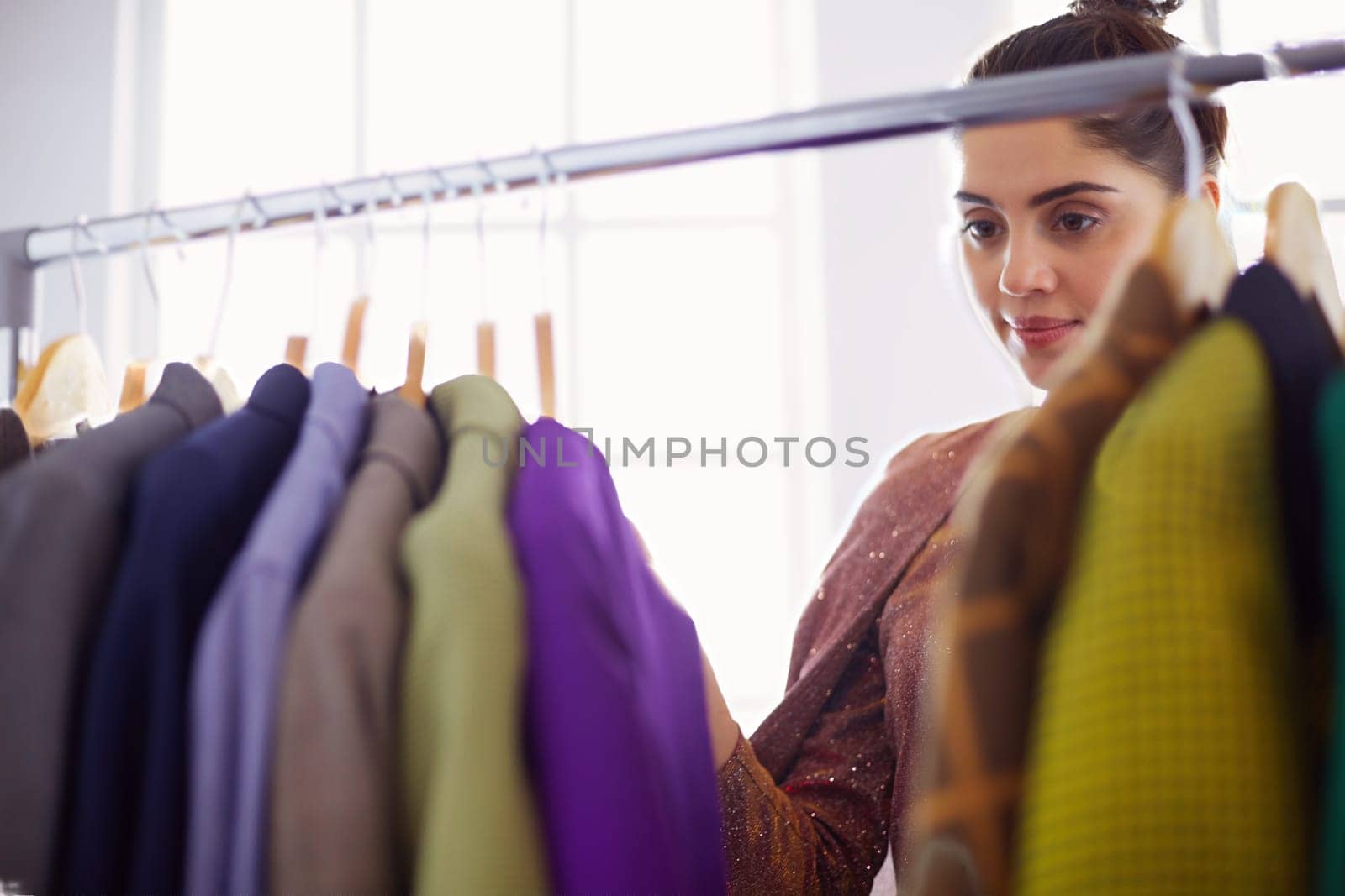 Beautiful young stylist near rack with hangers.