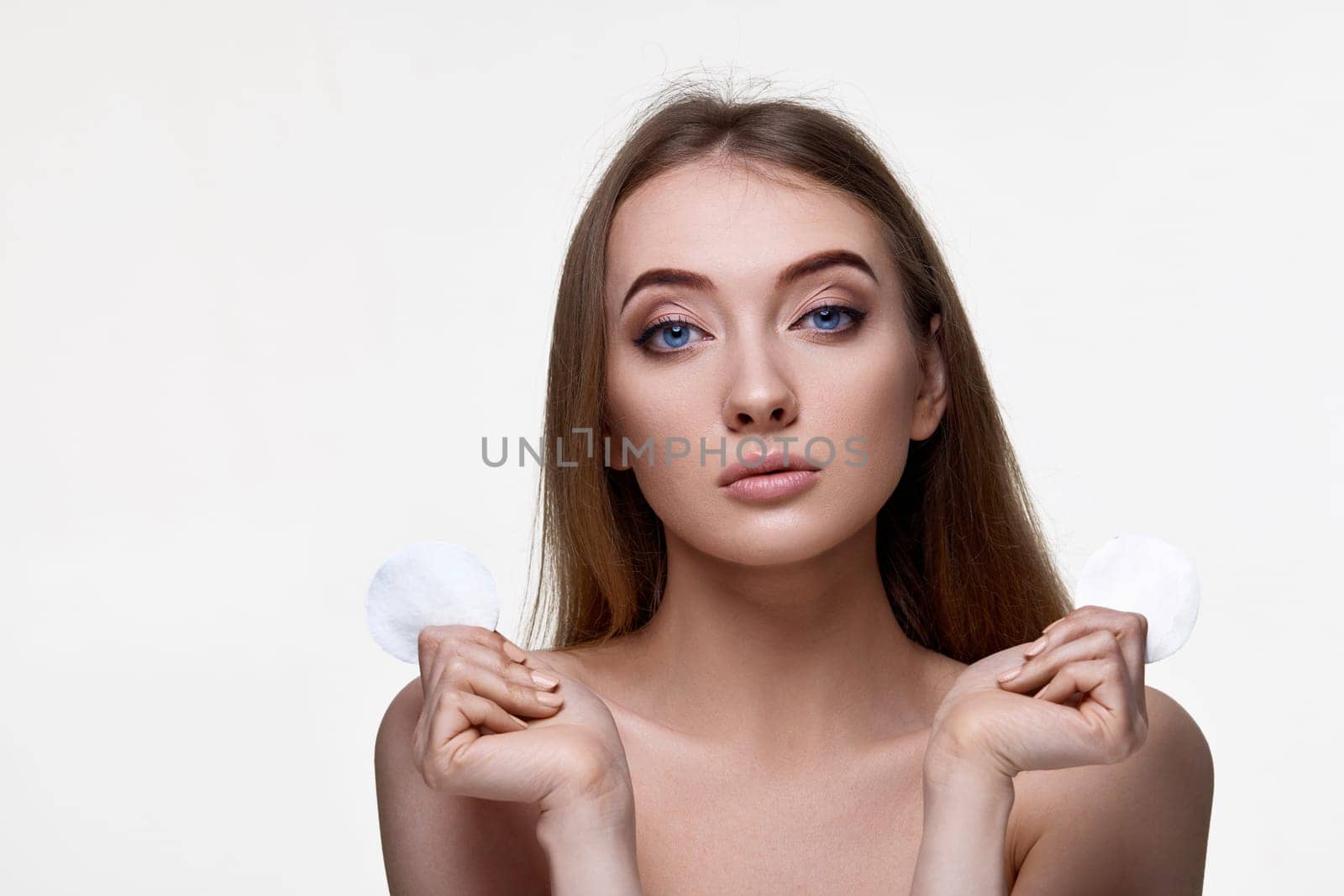 adorable woman holding two white cotton disks pad with micellar water on white background