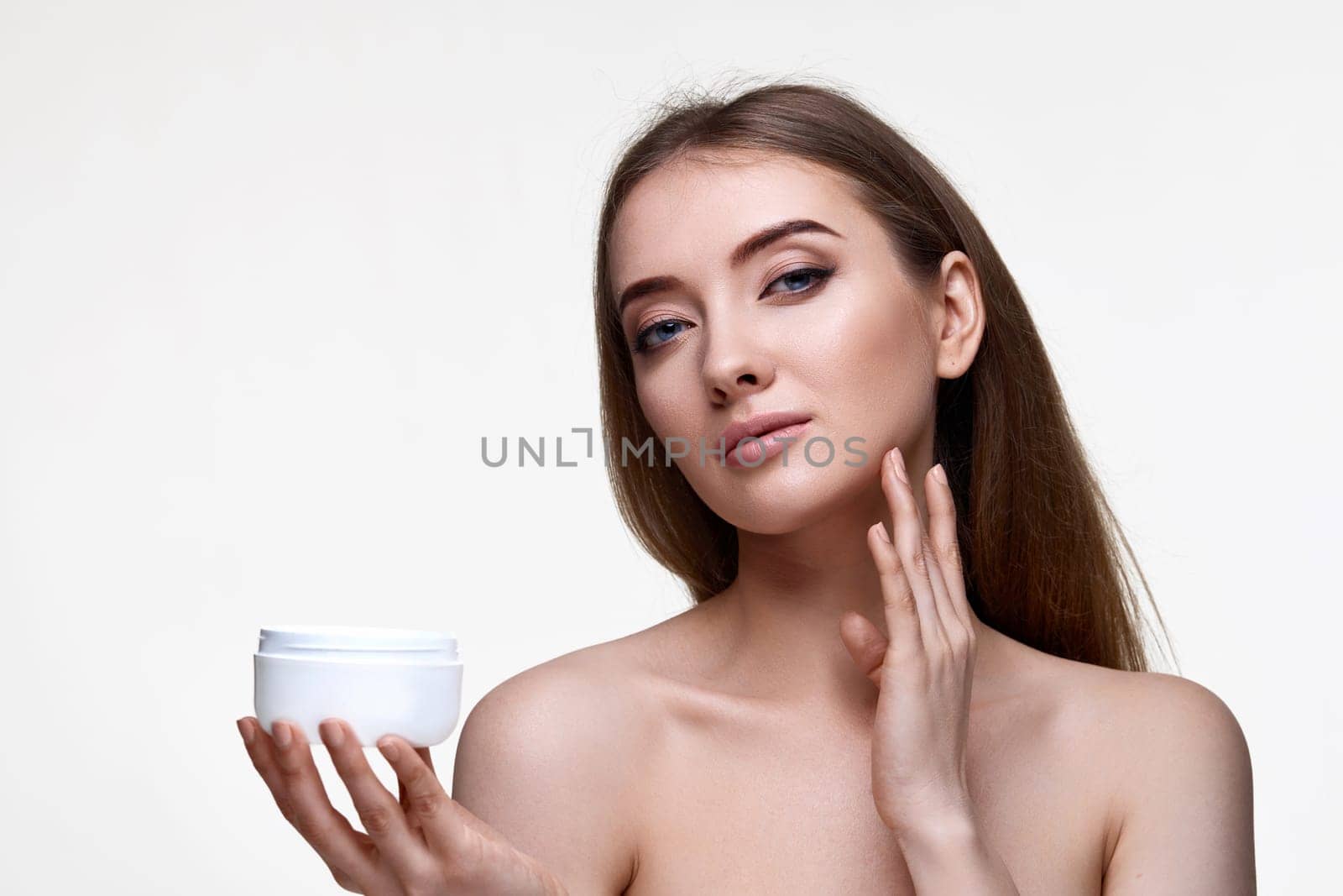 beautiful smiling young woman applying skin care cream on her face on white background
