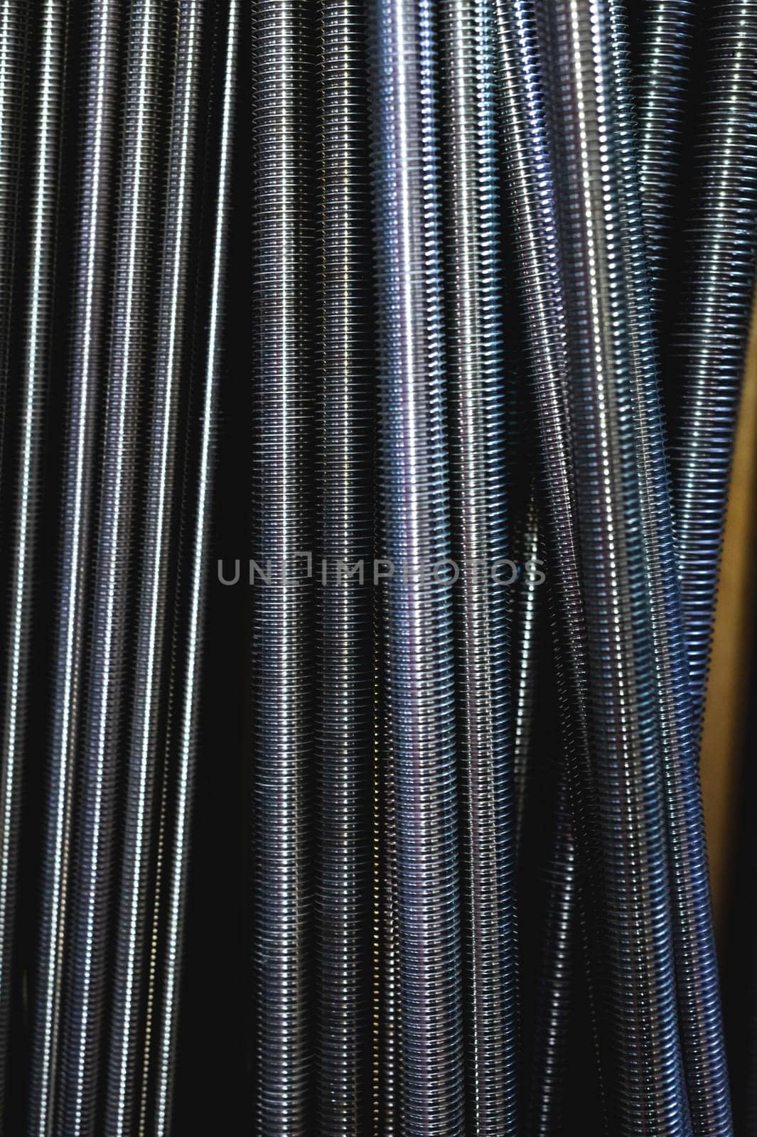Threaded rods are also called studs. Galvanized threads run along the entire length of the rod. They are used with a metal spacer when suspended from the ceiling. Inventory in an industrial warehouse.