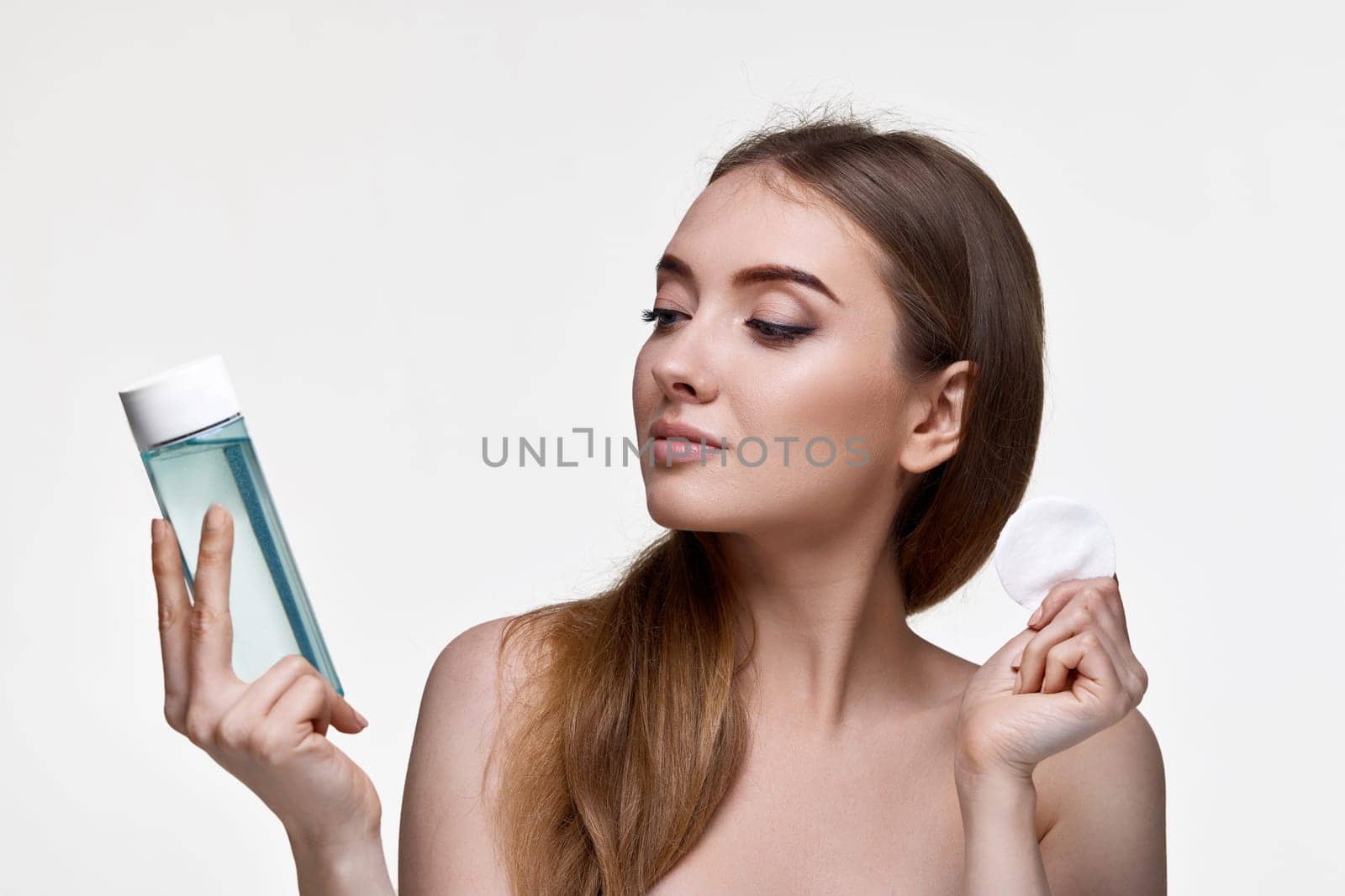 beautiful woman holding bottle with tonic, cleaning skin with cotton pad. Beauty and skin care concept