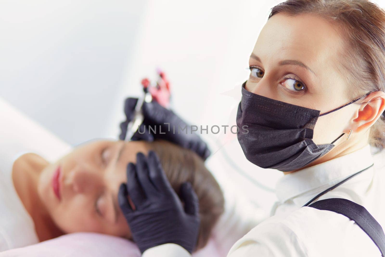 Young woman undergoing procedure of eyebrow permanent makeup in beauty salon by lenets