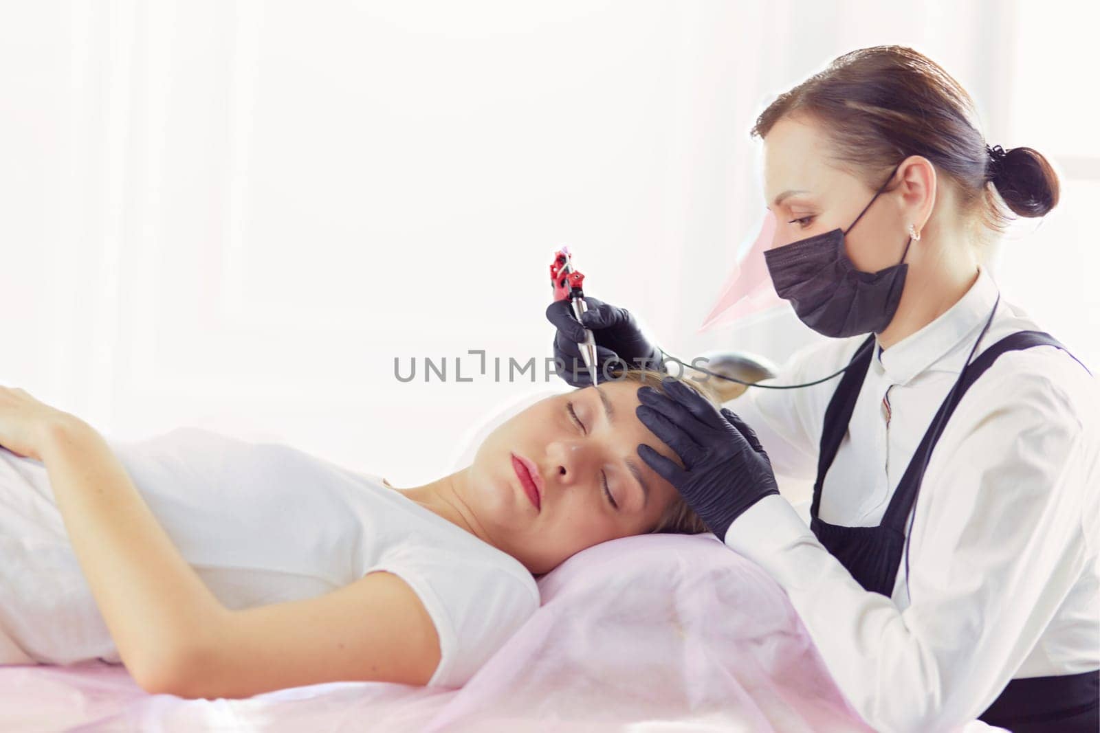 Young woman undergoing procedure of eyebrow permanent makeup in beauty salon.