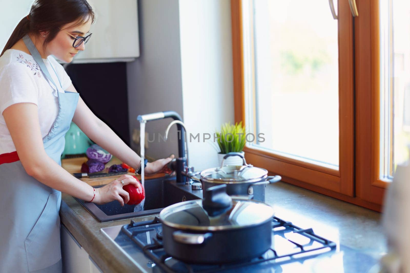Woman washing vegetables. Beautiful young woman washing vegetables for salad and smiling while standing in the kitchen.