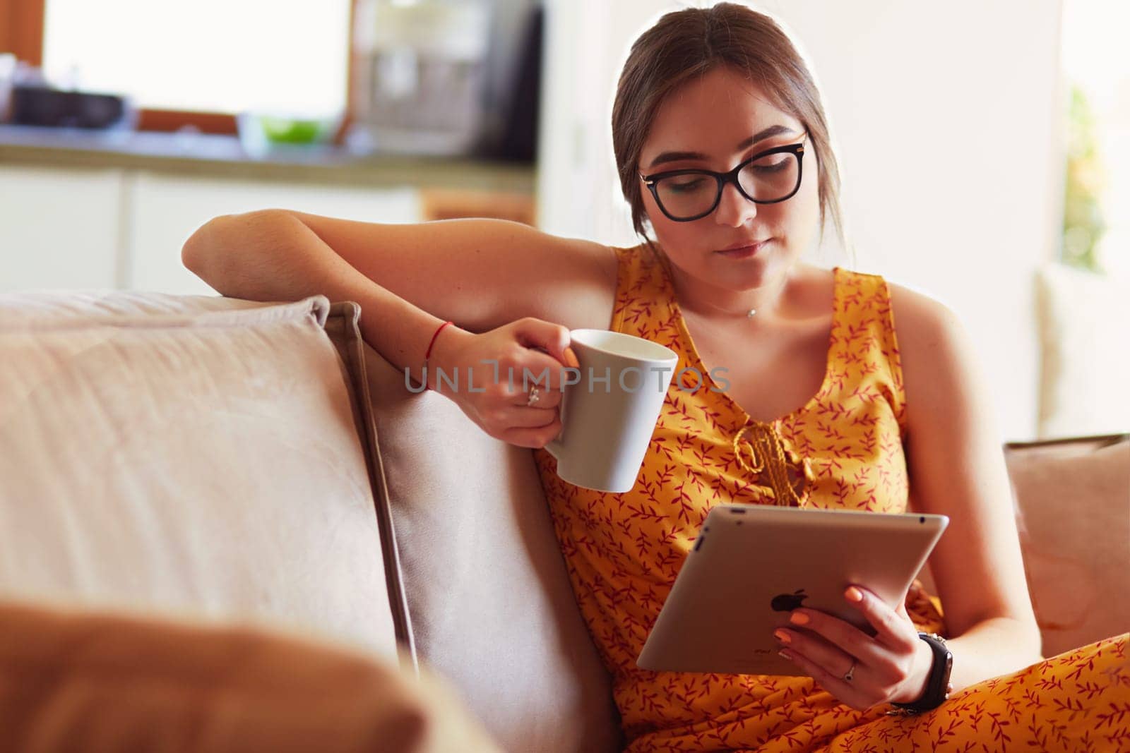 Young woman uses tablet while relaxing at home with coffee on the sofa couch.