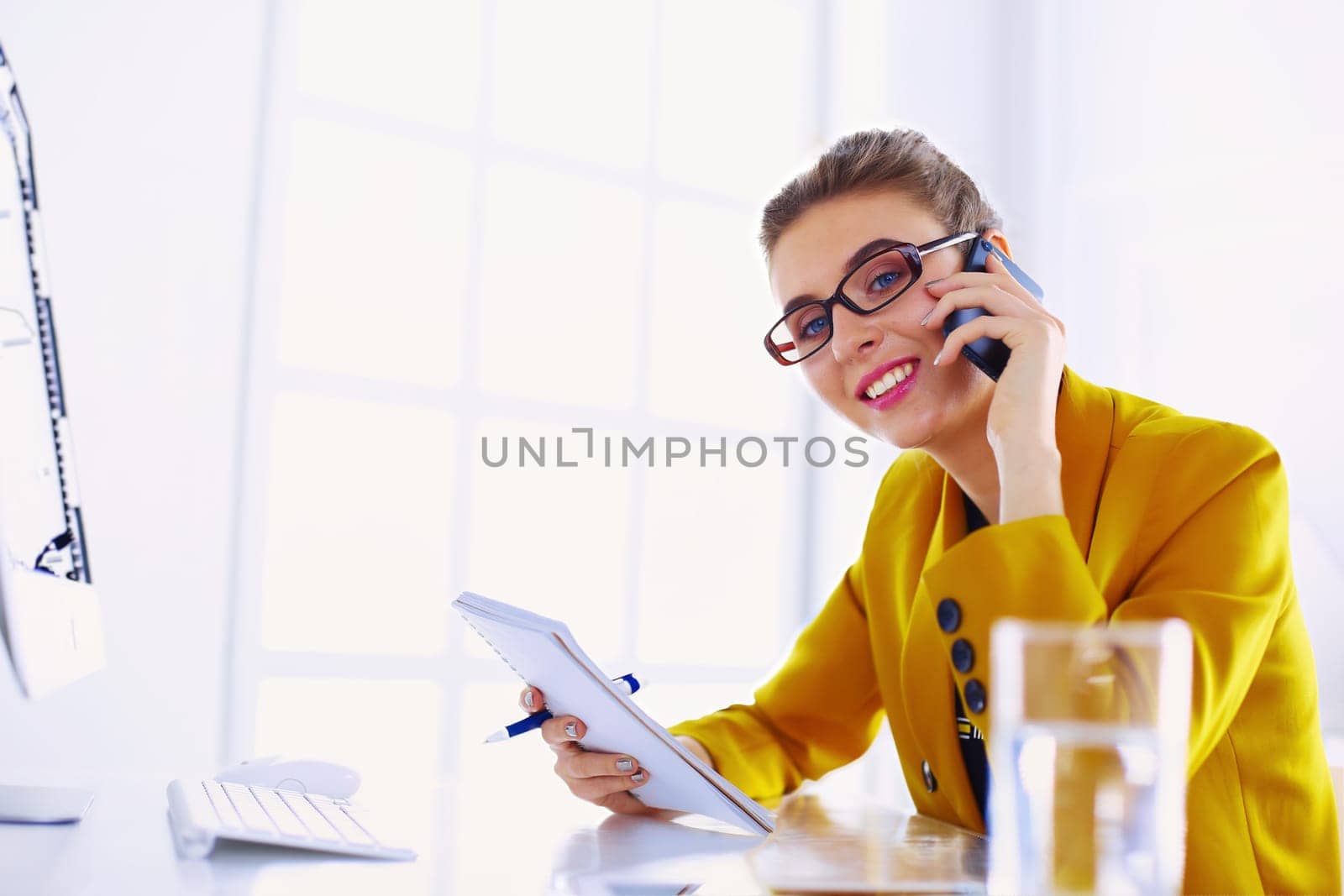 Portrait of beautiful woman making call while sitting at her workplace in front of laptop and working on new project