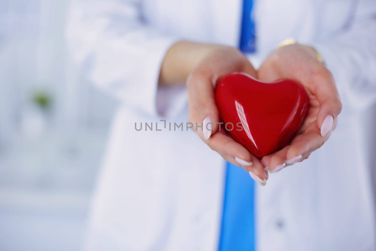 Female doctor with stethoscope holding heart, on light background.