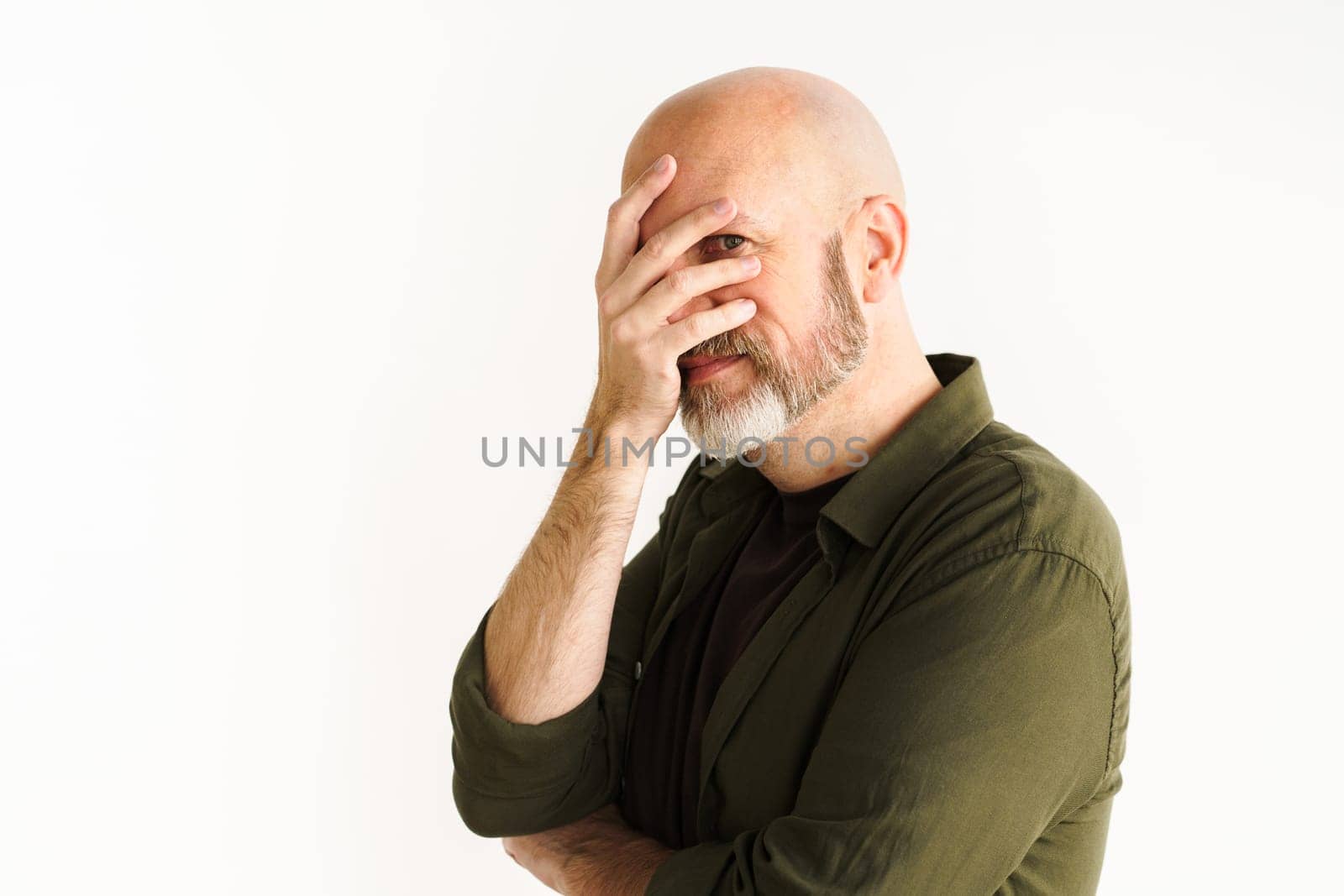 Mature man with silver beard in moment of frustration or disbelief. He puts hand on face in facepalm gesture, conveying sense of sarcasm and exasperation. White background adds emphasis to reaction. High quality photo