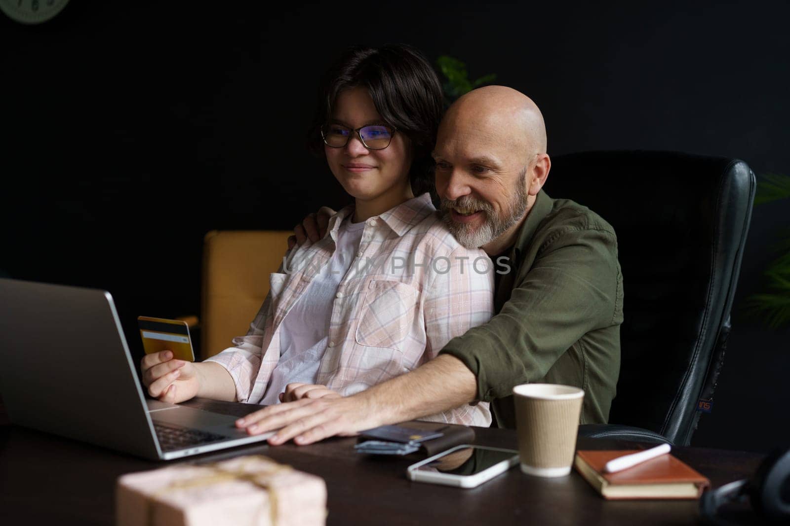 Joyous bond between happy father and teenager daughter. Online shopping experience, engaging in shared activity. Father holding credit card in hands, ready to enter payment data for purchase. . High quality photo