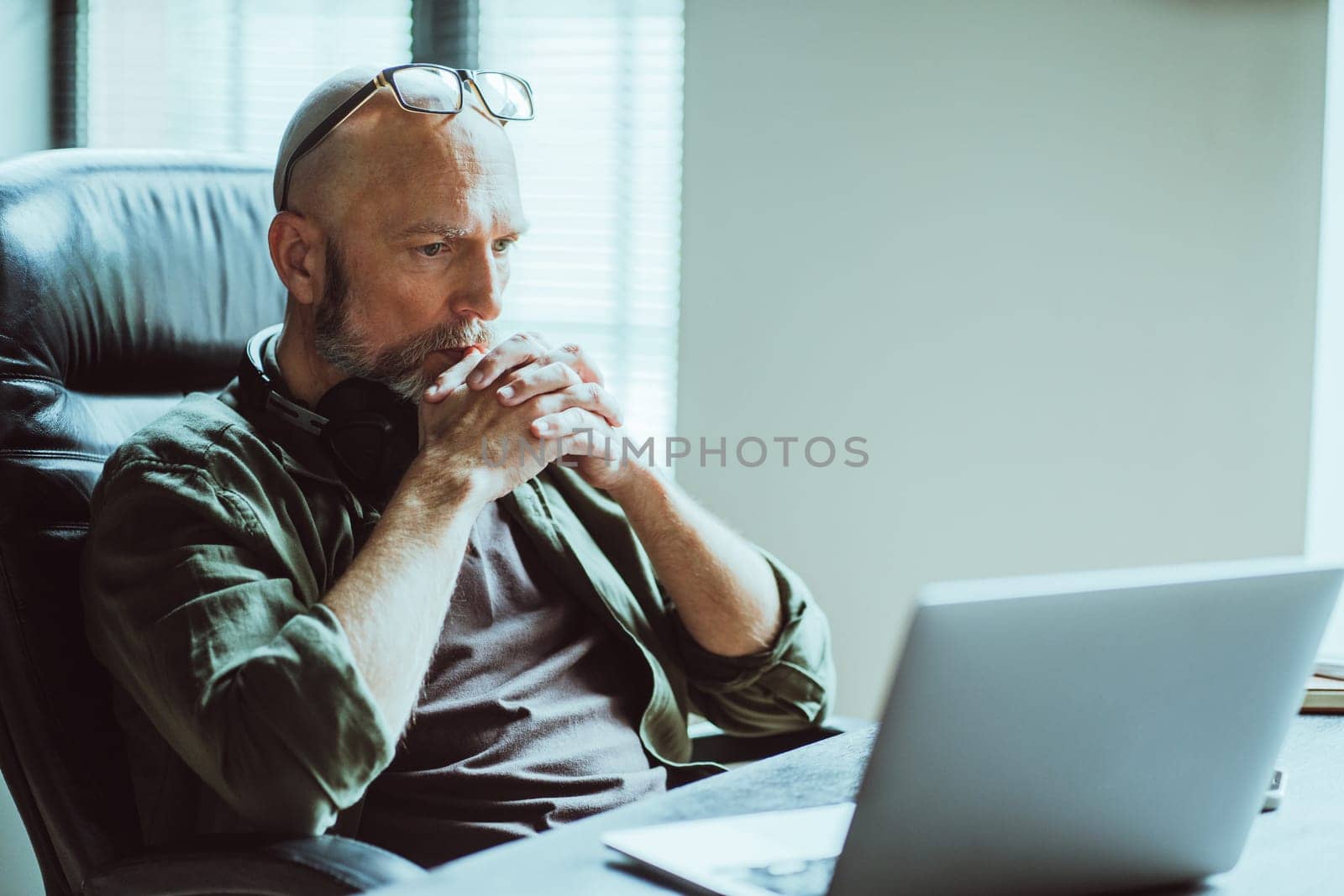 Middle-aged man fully focused on work he looks intently at computer on table. Deep in thought, he reflects on task or problem at hand, demonstrating his analytical and strategic thinking skills. by LipikStockMedia