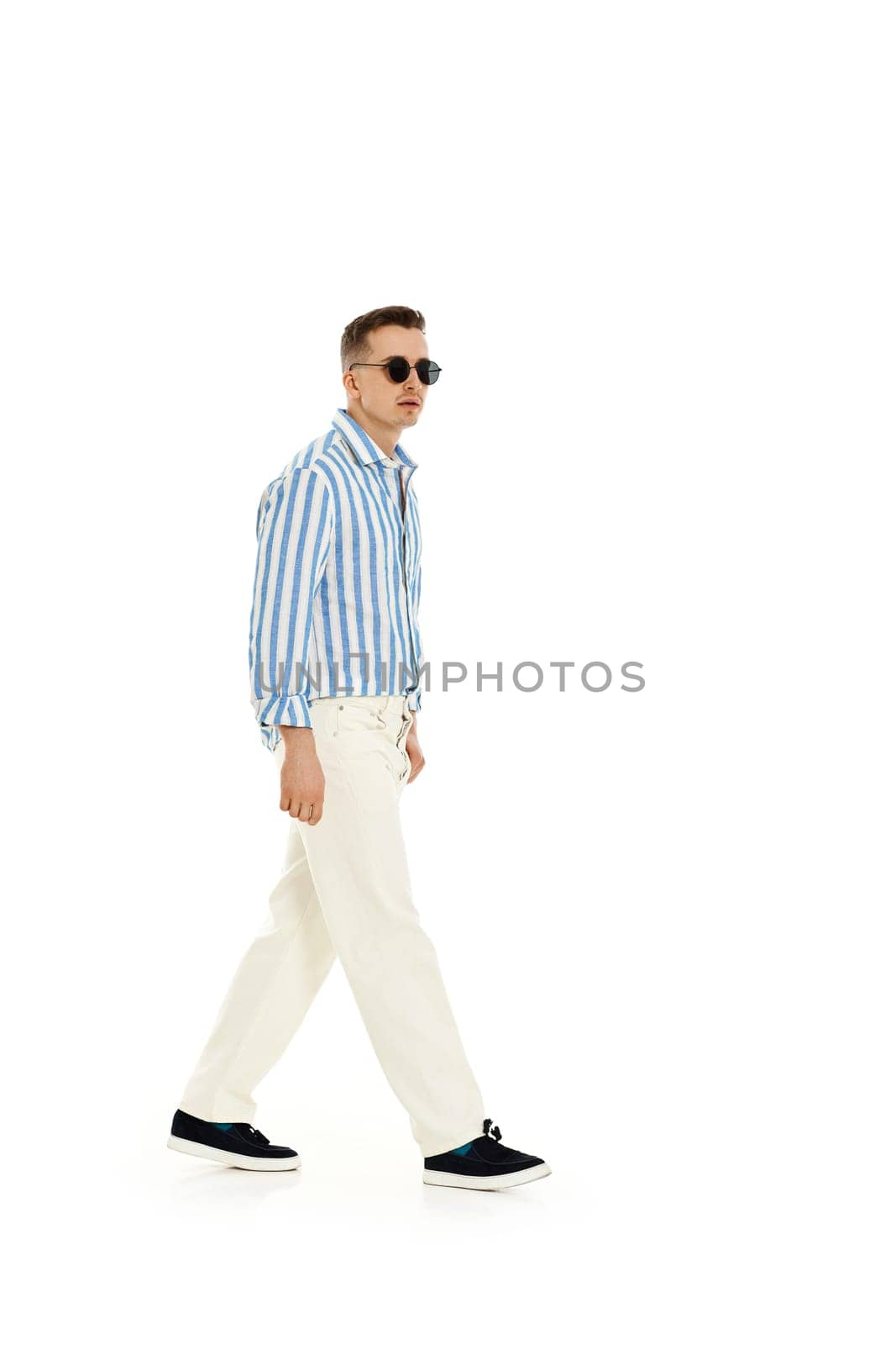 Smiling happy confident man in sunglasses and blue striped shirt standing isolated on white background. full length. Summer fashion