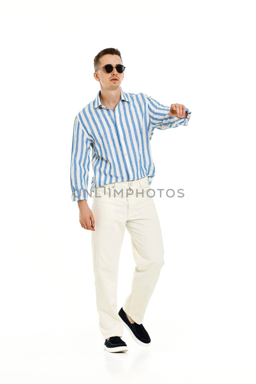 Smiling happy confident man in sunglasses and blue striped shirt standing isolated on white background. full length. Summer fashion