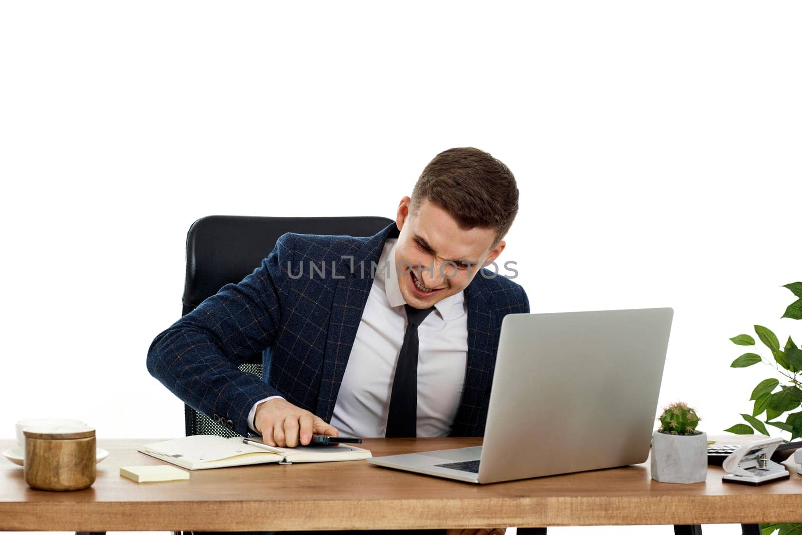 Upset angry businessman sitting on chair at desk after talking on the phone, using laptop