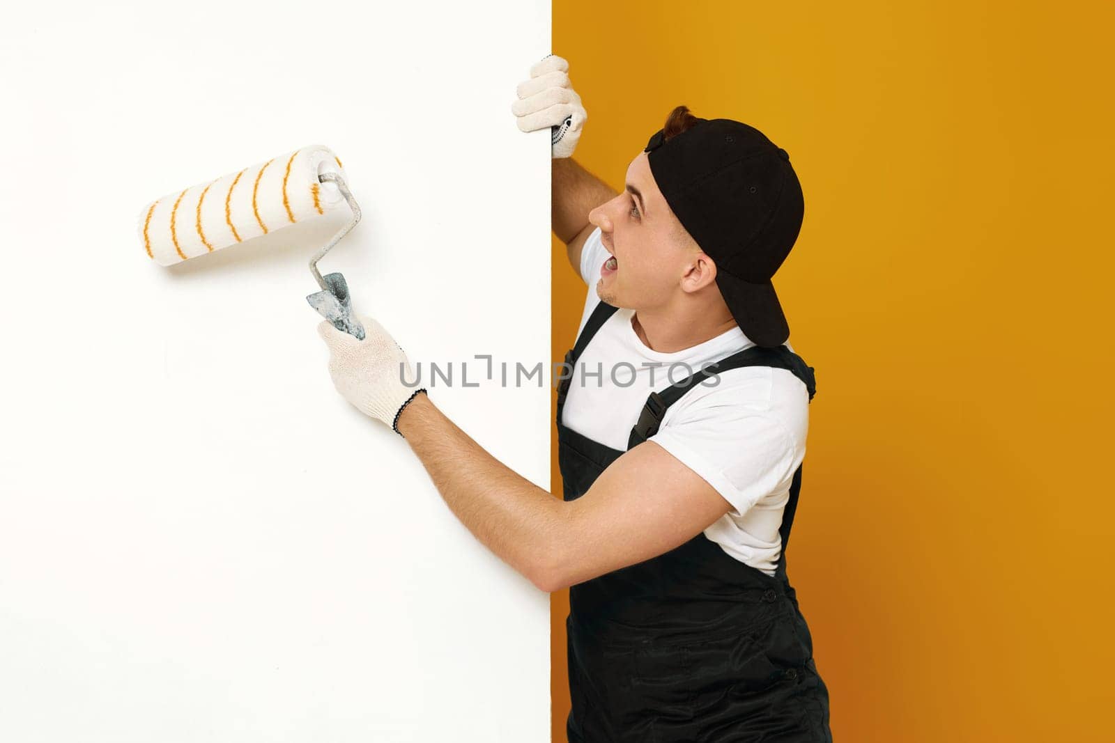 worker handyman in working clothes painting white walls in the room. copy space for text
