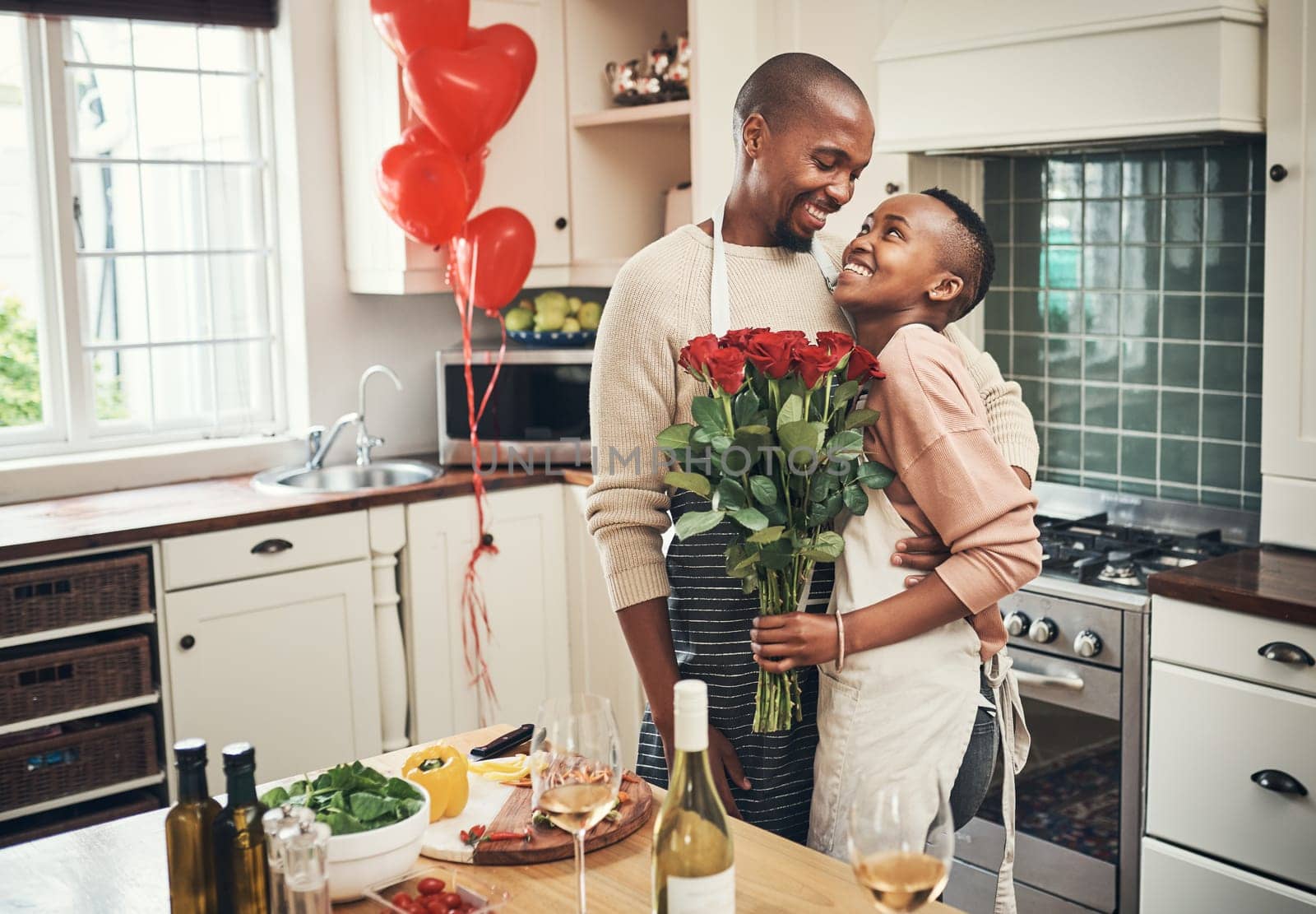 Flowers, love and valentines day with a black couple in the kitchen for a romantic celebration together. Food, gift or romance with a man and woman bonding in their home during a special event by YuriArcurs