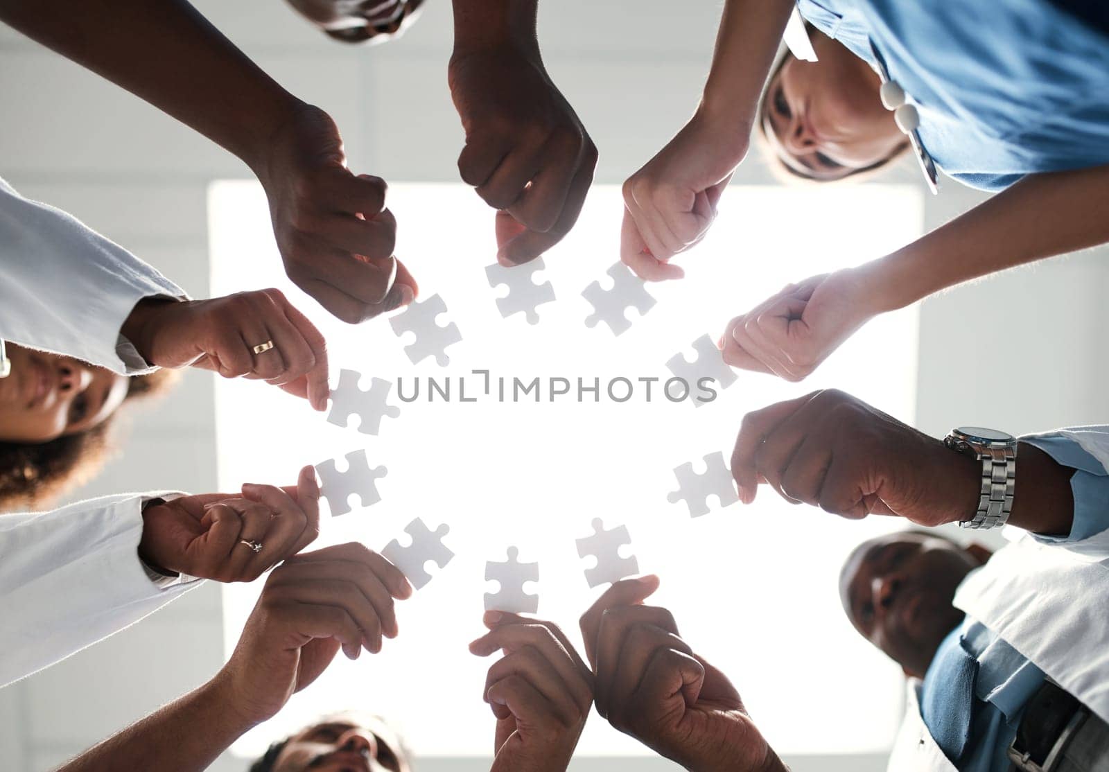 Piecing together ways to provide a better healthcare service to all. Low angle shot of a group of medical practitioners joining puzzle pieces together. by YuriArcurs