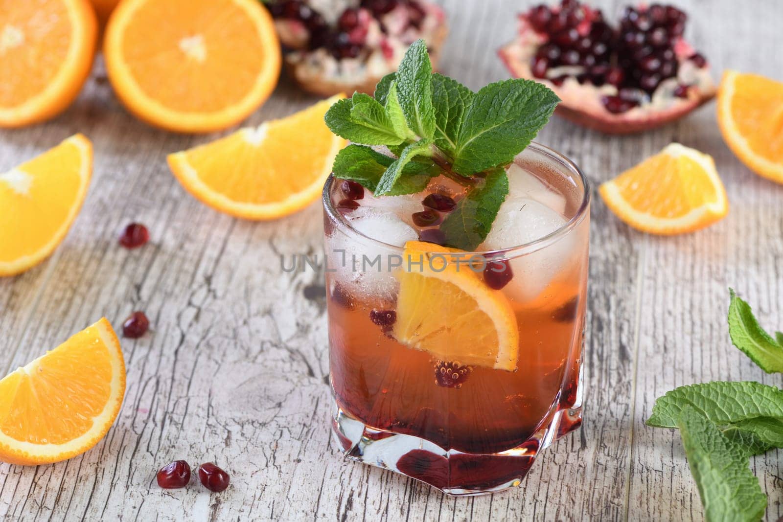 The cocktail is made from pomegranate and orange juice with tequila or gin, with the addition of tonic. Served in a glass with ice, orange slices with pomegranate and a sprig of mint. Cocktail recipe for any party.