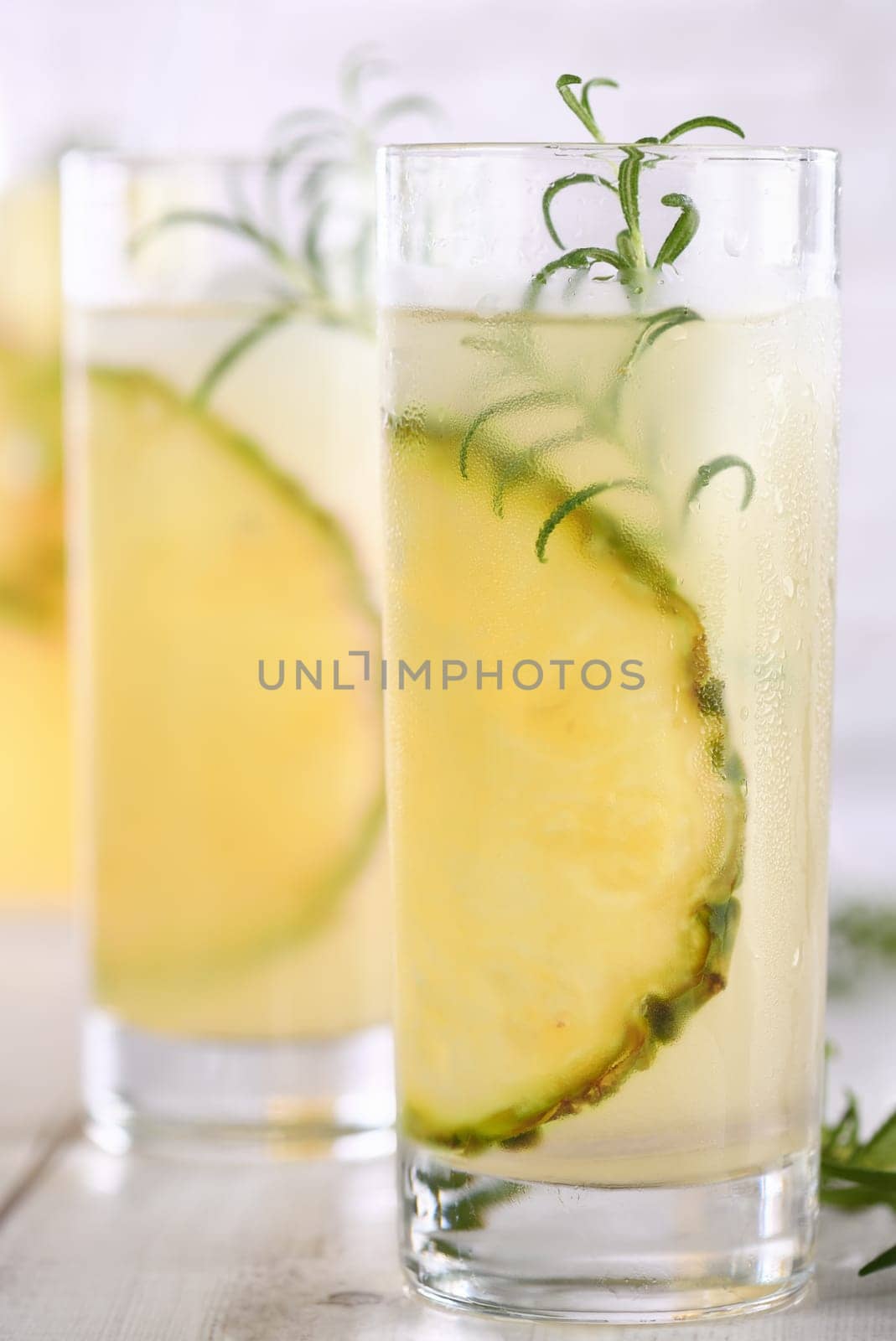 A glass of lemonade with pineapple pieces, ice cubes and rosemary. Cold refreshment organic non-alcohol cocktail.