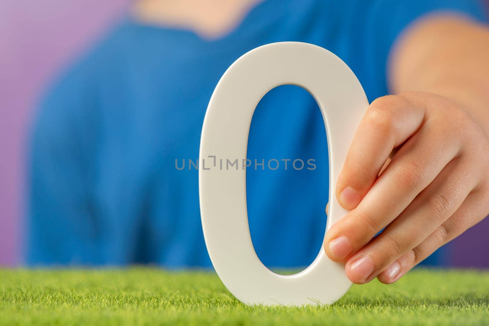 Number 0 in hand. Hand holding white number zero over green grass and purple background, concept of zero emission CO2, interest rates, zero score in the game. copy space. High quality photo