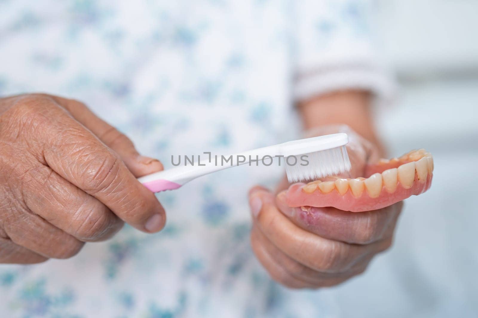 Asian elderly woman patient use toothbrush to clean partial denture of replacement teeth.