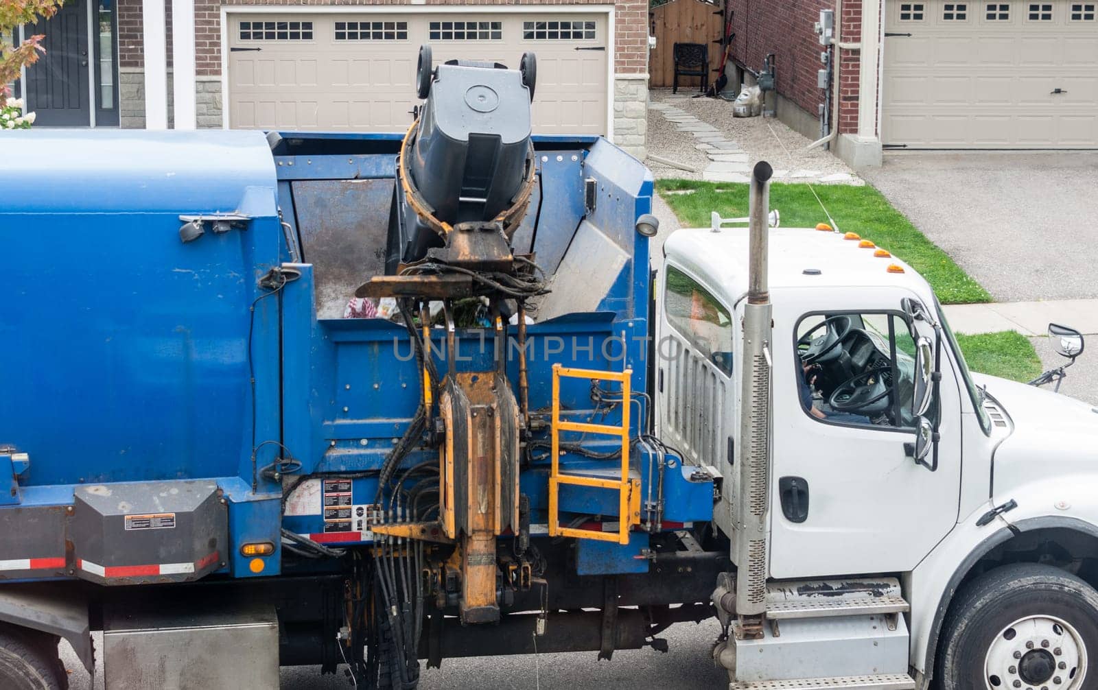 A mechanical hand lifts a standing rubbish bin and loads it into the desired section of the garbage truck