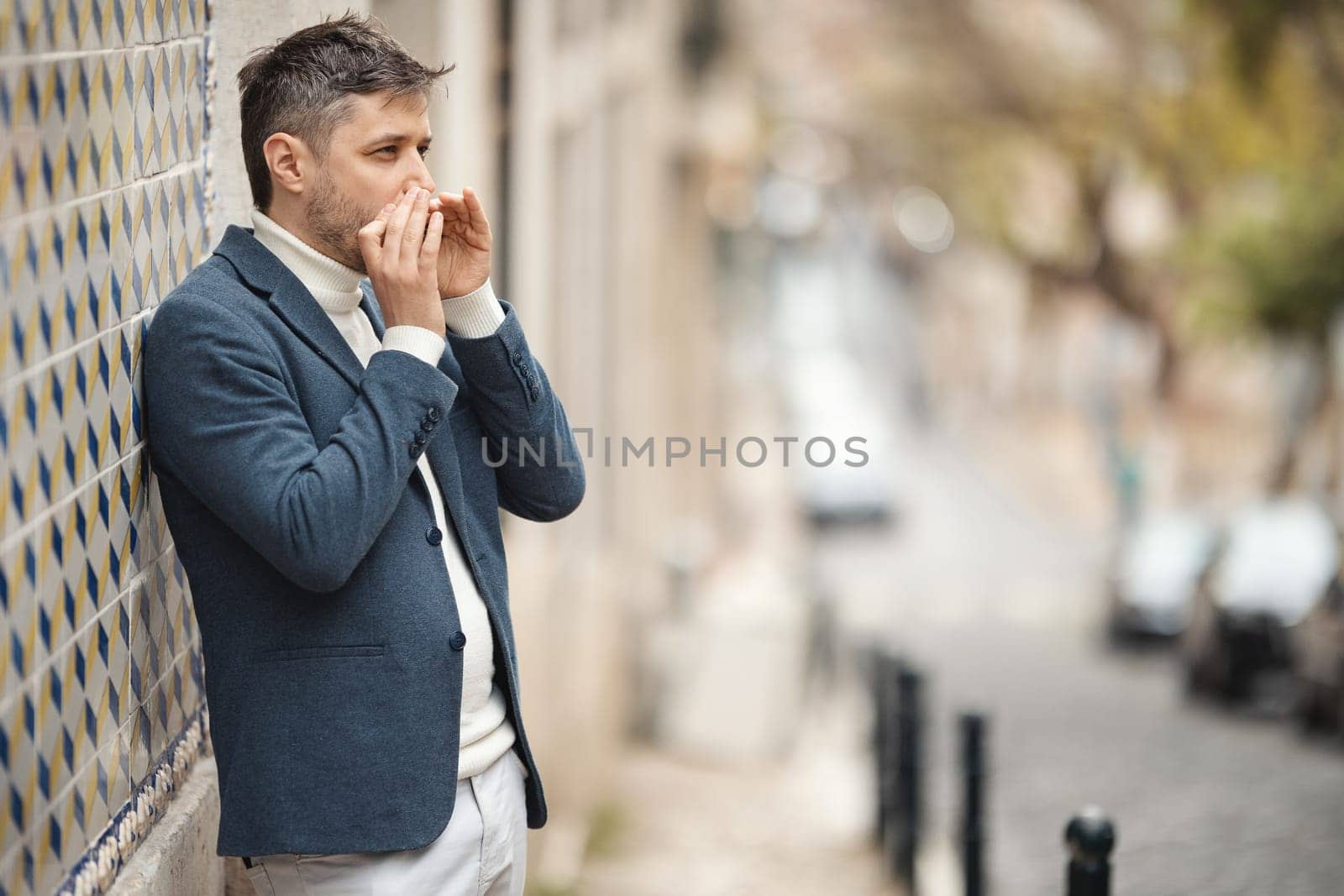 A man stands against the wall and plays the harmonica in the street. Mid shot