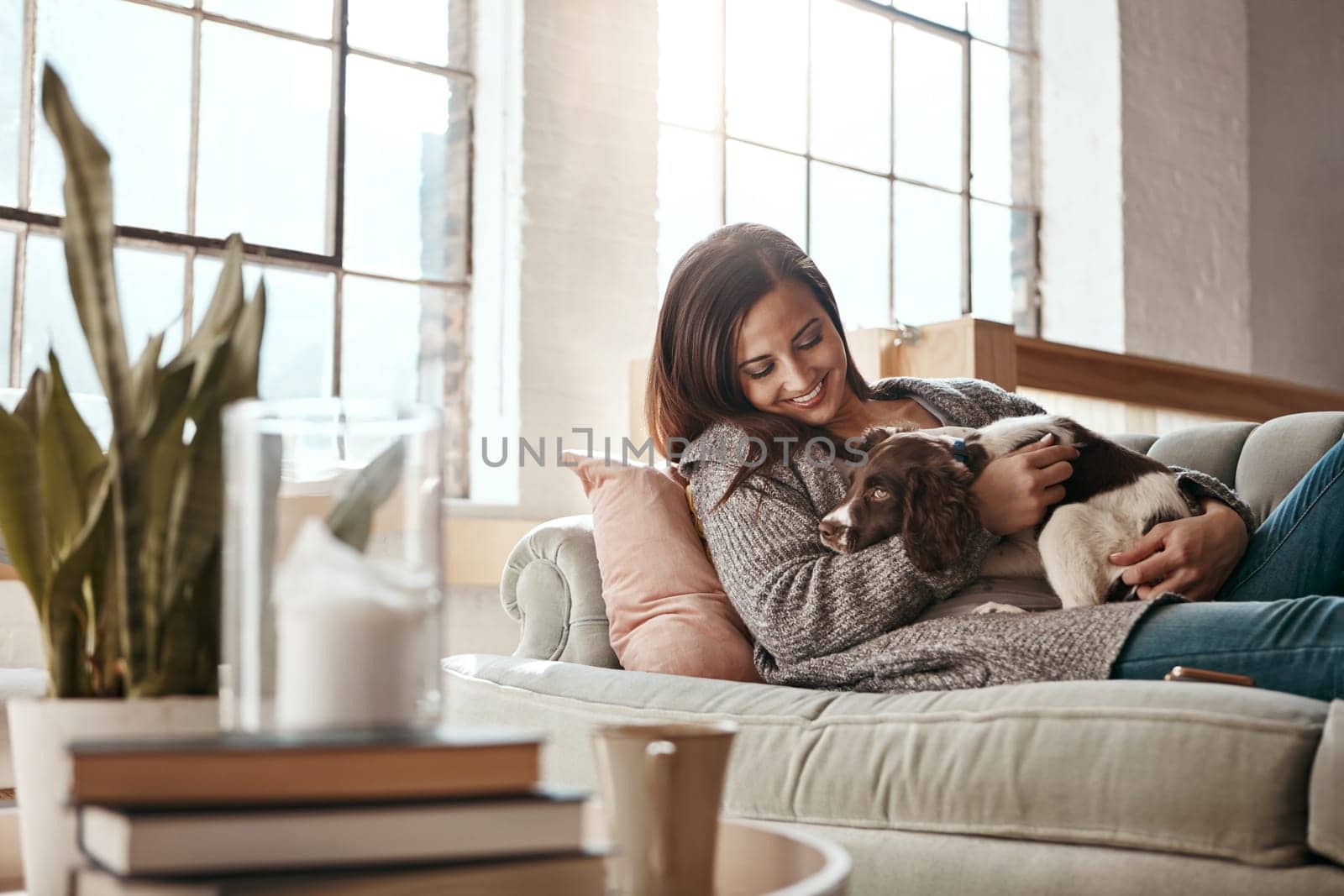 Woman relax on couch with puppy, happy and content at home with pet, happiness together with peace in living room. .Female cuddle dog, love for animals with smile and care, stress relief and comfort by YuriArcurs